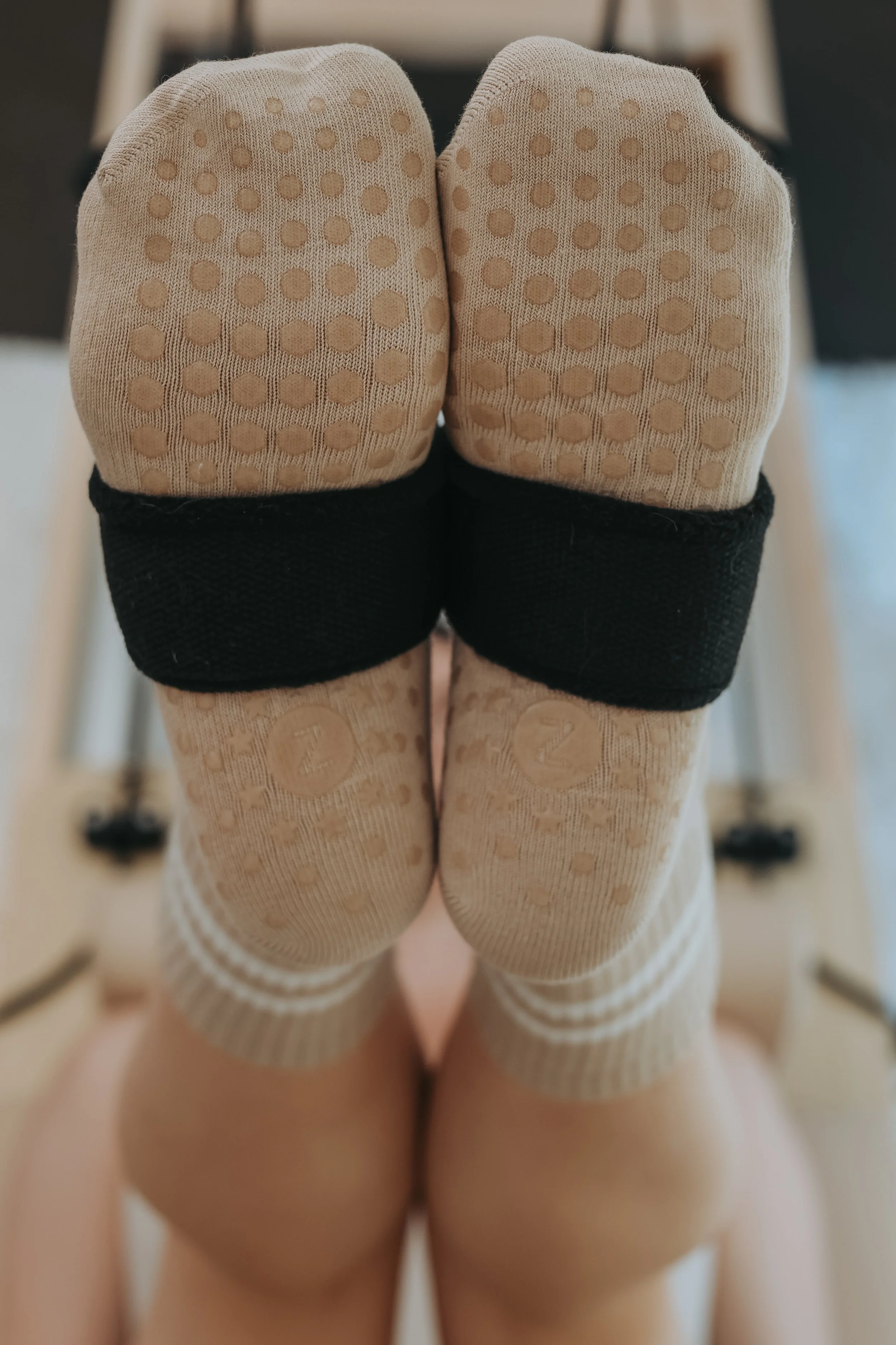 Close-up of person's feet wearing beige socks with dotted grips, with a black band at the top, and folded over knees in the foreground.