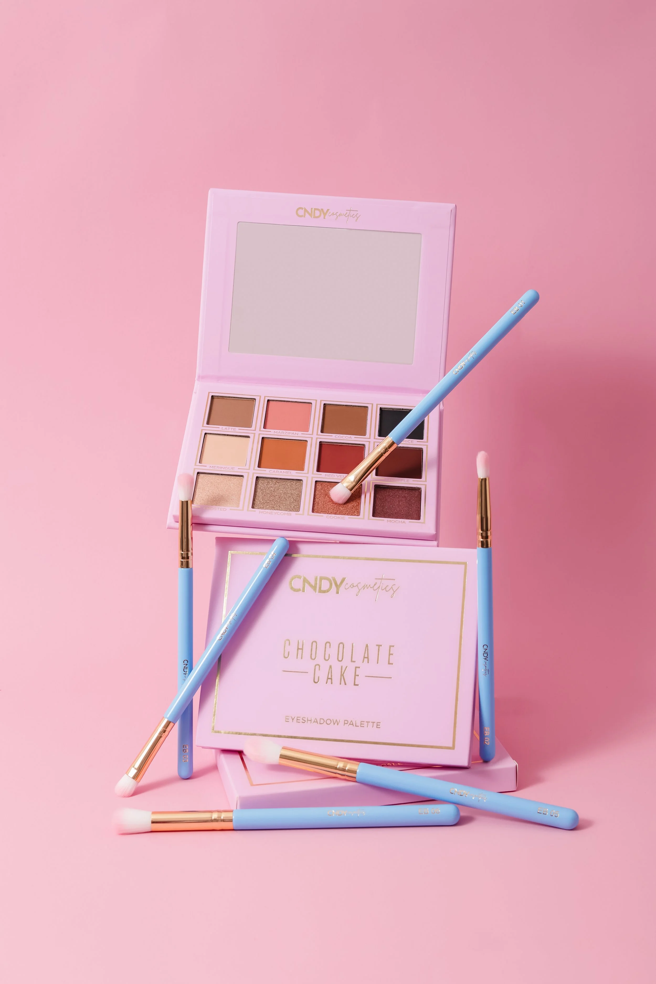 Pink eyeshadow palette with various shades and brushes on a pink background.