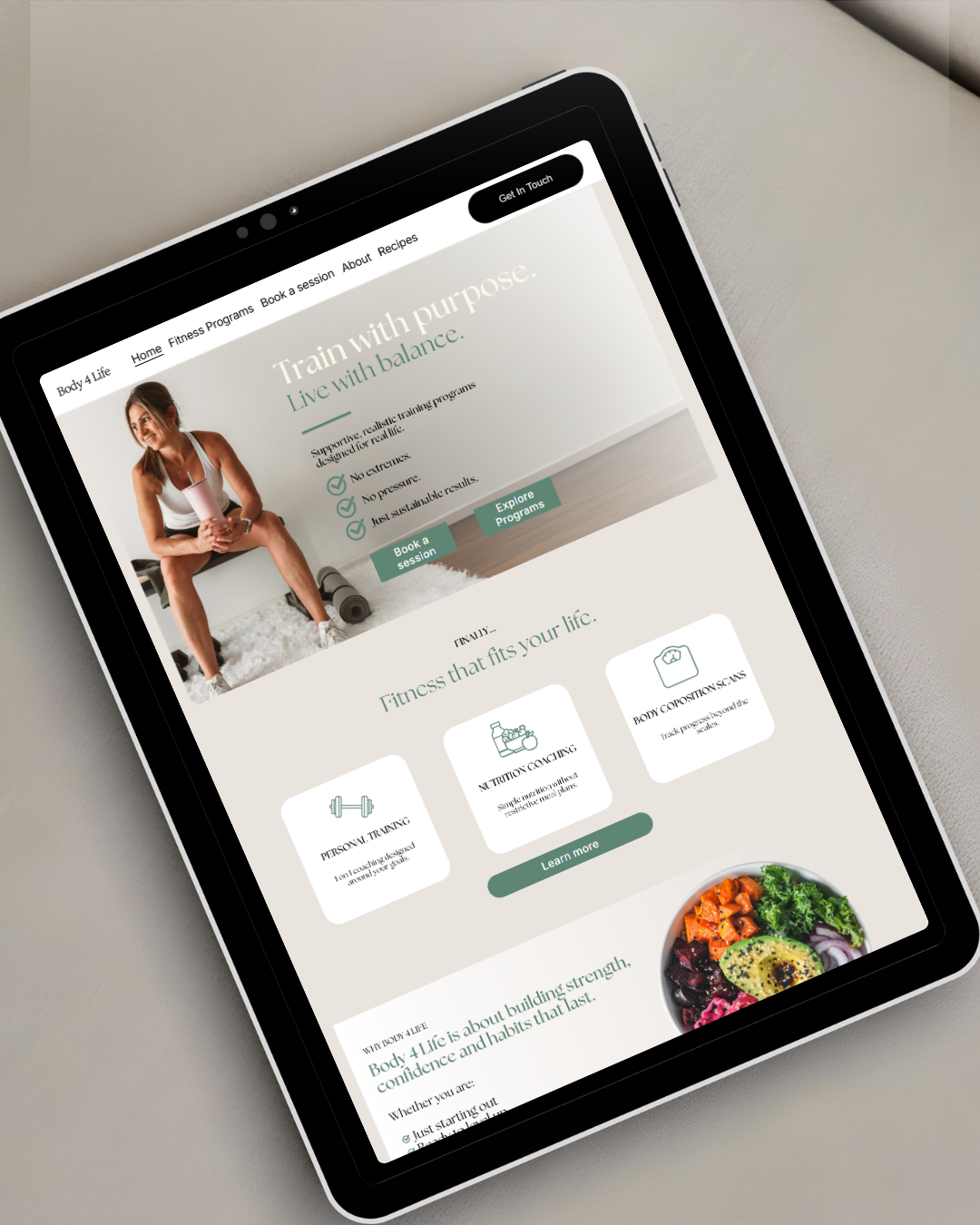 Tablet displaying a fitness website with a woman sitting on a workout bench, smiling and holding a shaker bottle, alongside text about training with purpose and healthy lifestyle options.