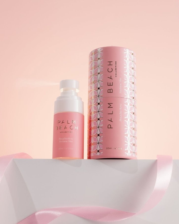 Two pink bottles of Palm Beach collection perfume on a white display shelf with a pink ribbon, set against a light pink background.