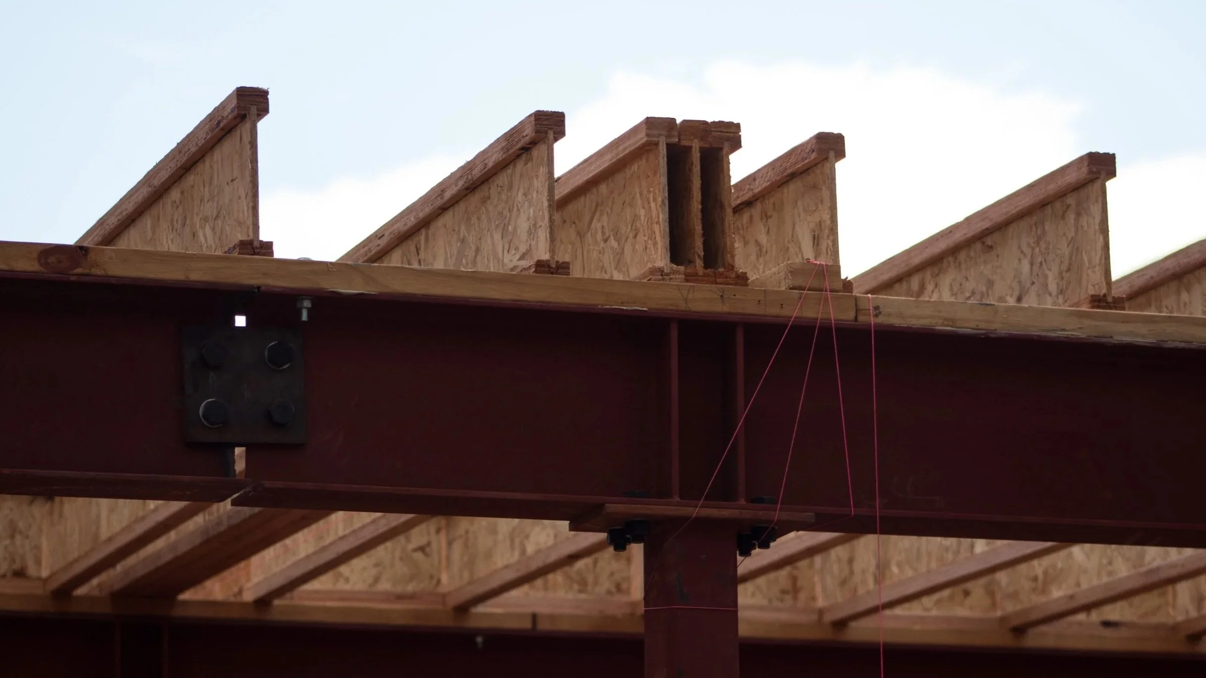 Close-up of a roof structure under construction, showing wooden rafters and plywood sheathing, with red string lines for alignment.