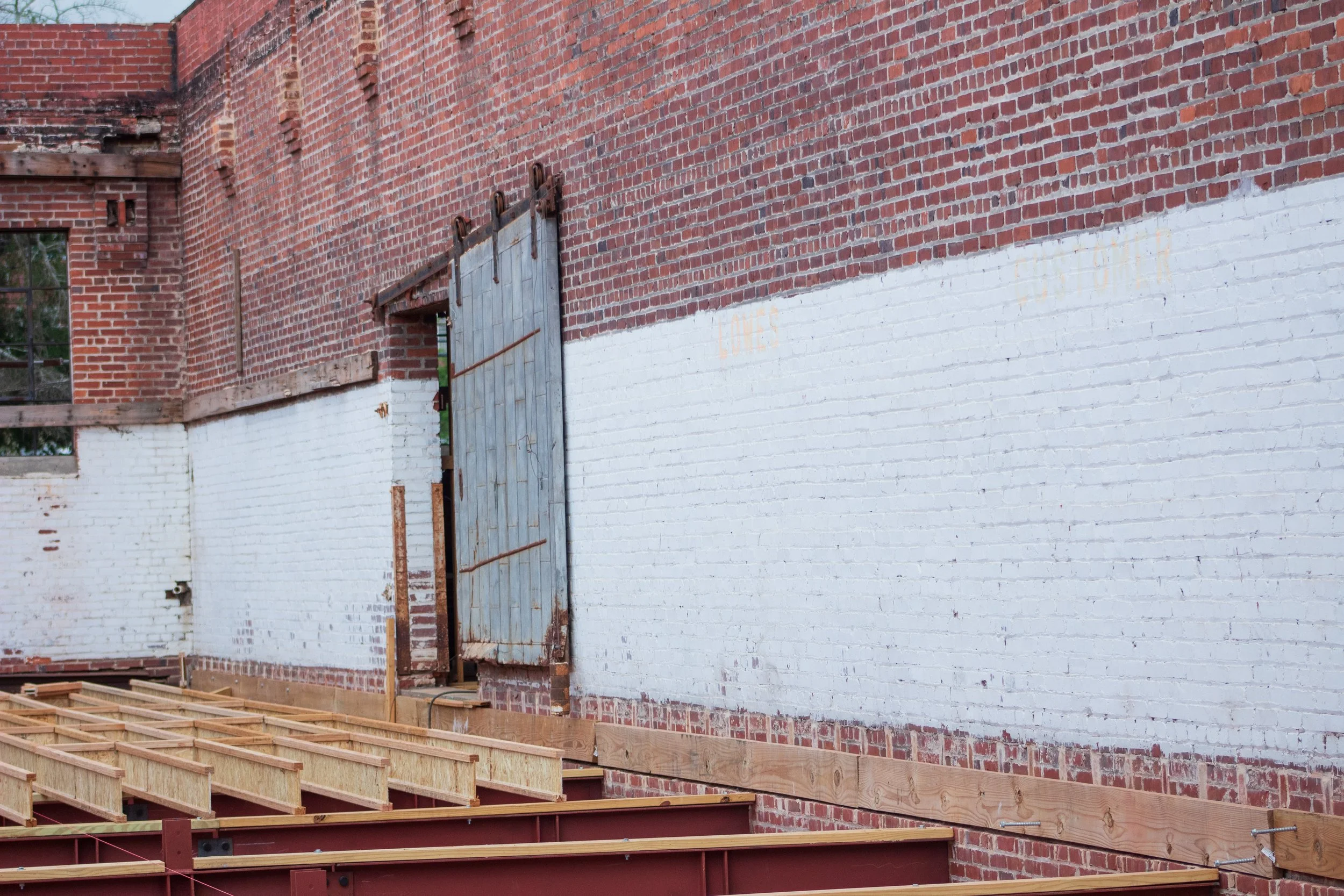 Construction site with brick walls, a large open doorway, and wooden framing for a new building.