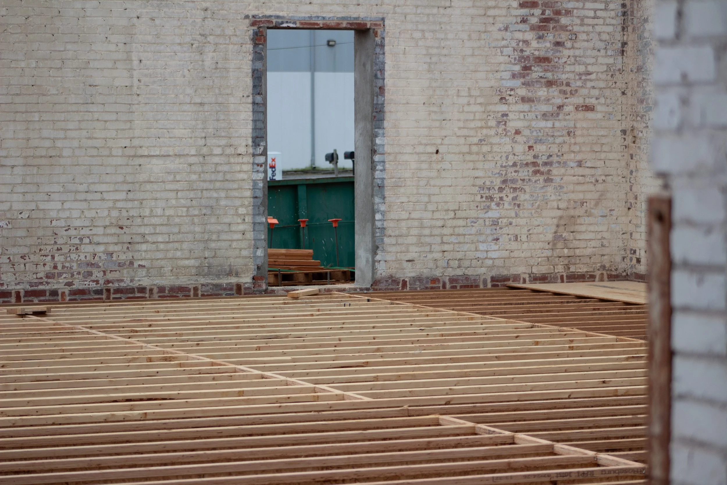 View of a wall with an opening, showing construction materials inside, including a FedEx container and wooden floor framing.