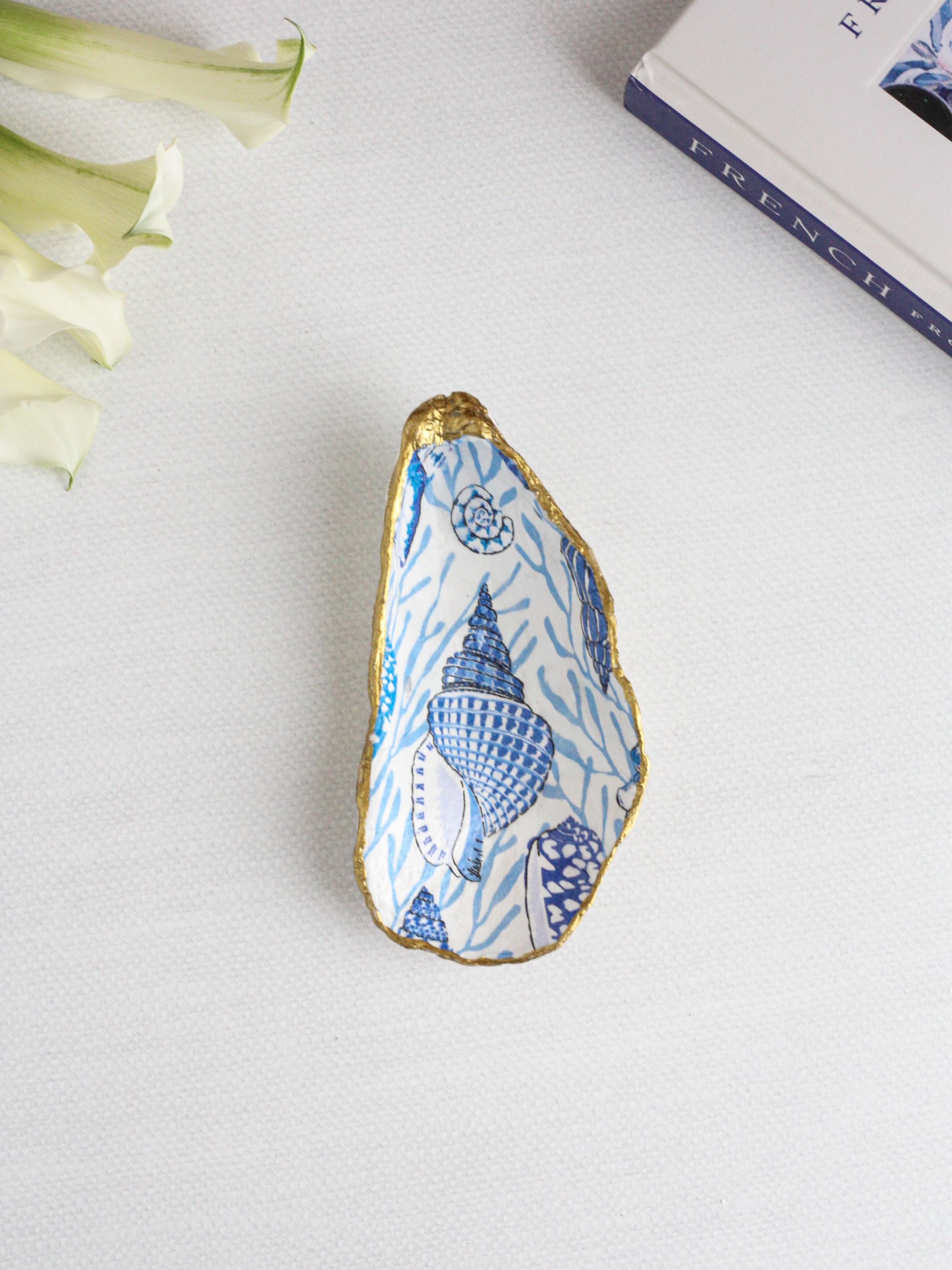 Azure Oyster Ring Dish 🐚

Handcrafted from a natural oyster shell and finished with delicate blue and white coastal artwork, the Azure Oyster Ring Dish brings timeless French coastal elegance to your everyday. Perfect for rings, earrings, and life&r