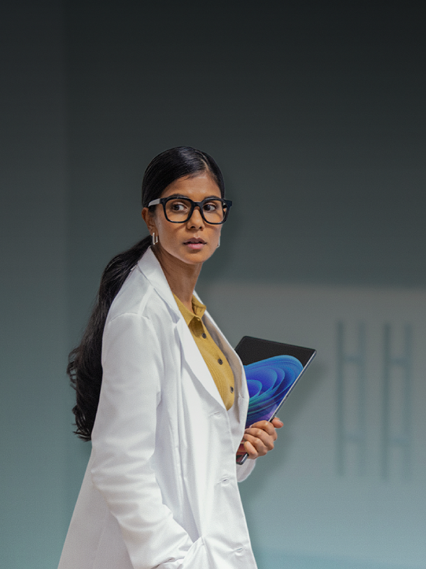 A woman in a lab coat holding a microsoft surface tablet looking over her shoulder