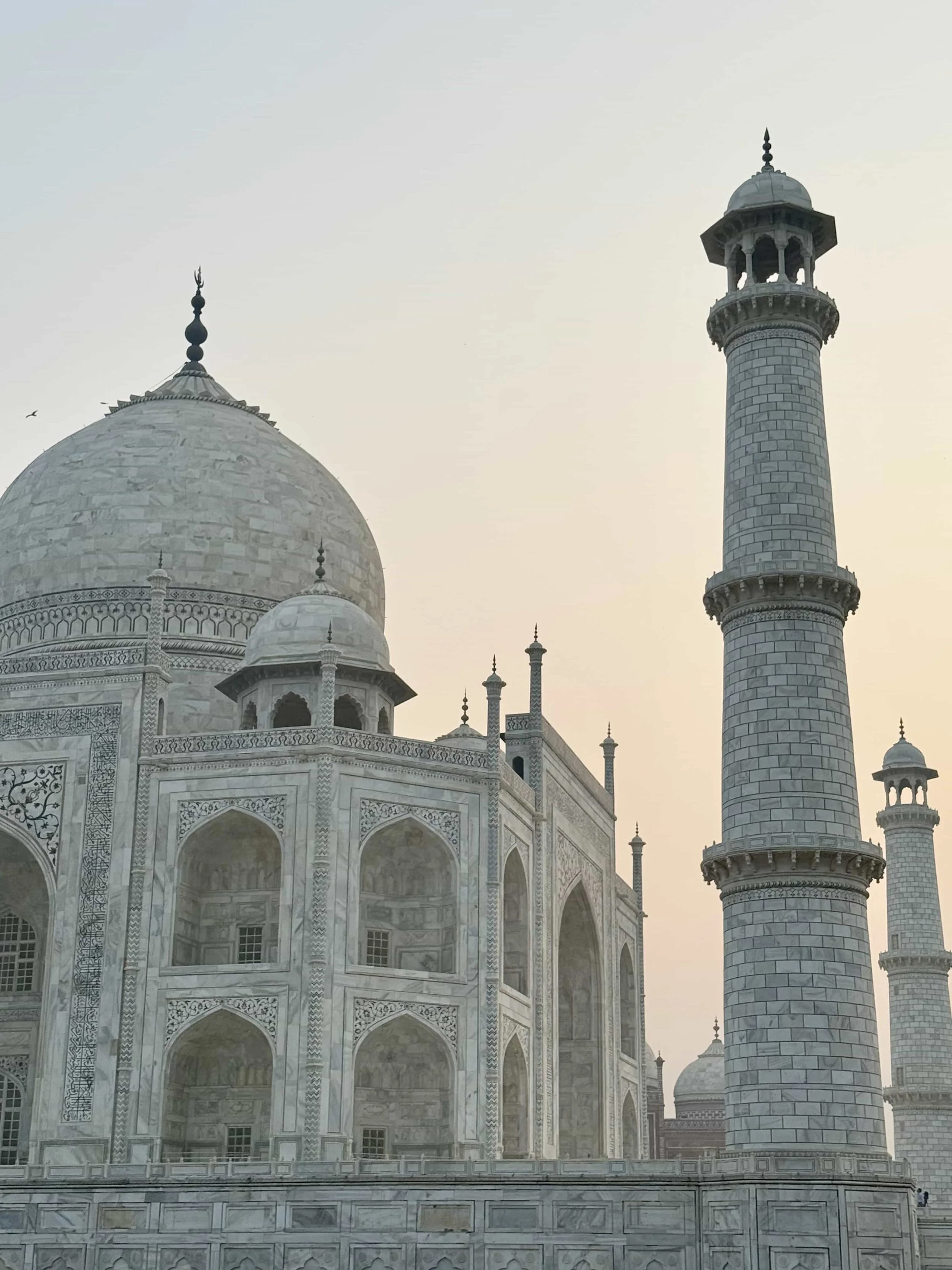 White marble monument with domes and tall minarets, featuring intricate carvings, set against a pale sky