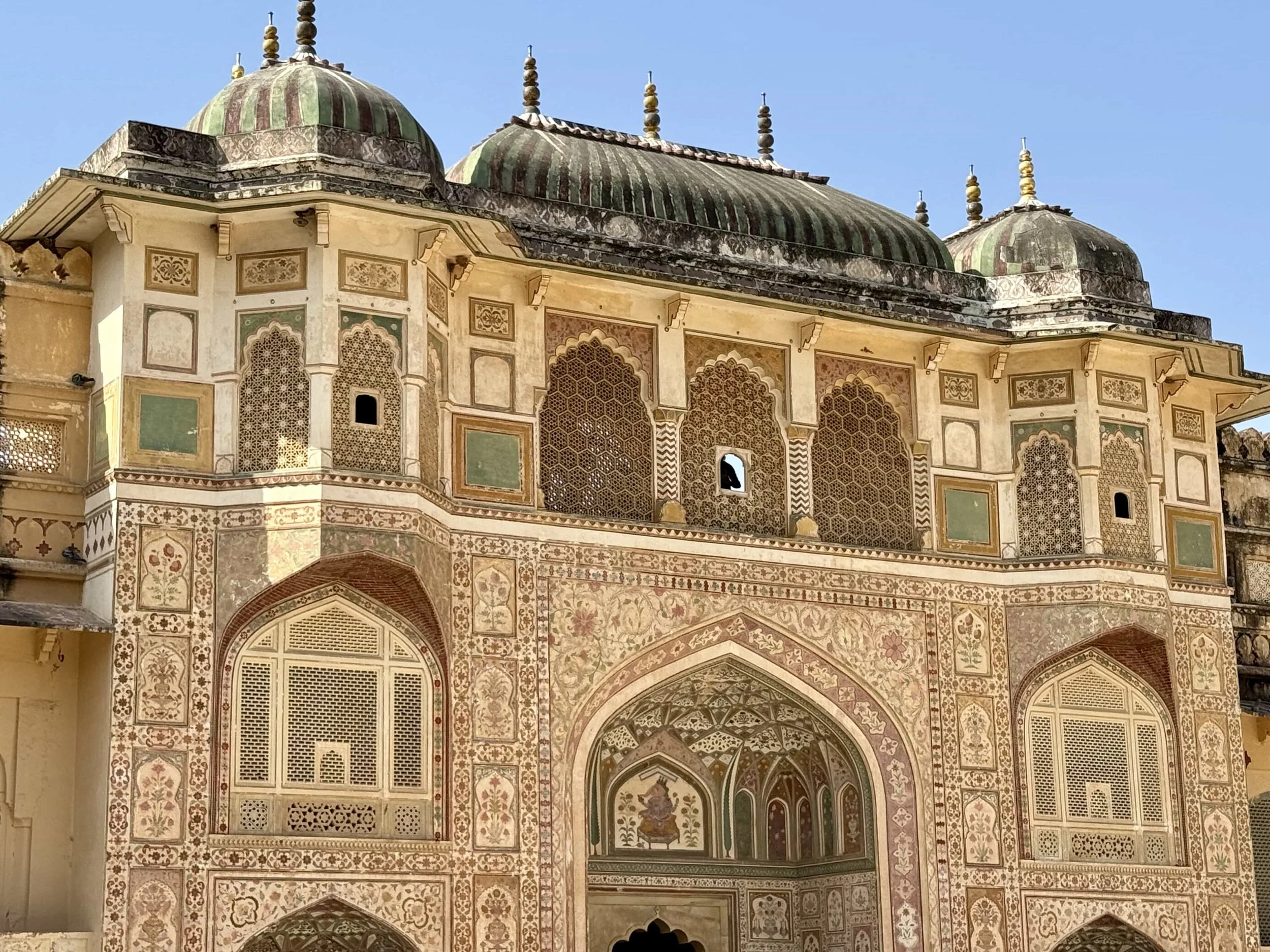 Close-up of decorated architecture on a historical building, featuring ornate patterns, arched windows, and domed roofs with finials, showcasing traditional Indian craftsmanship.