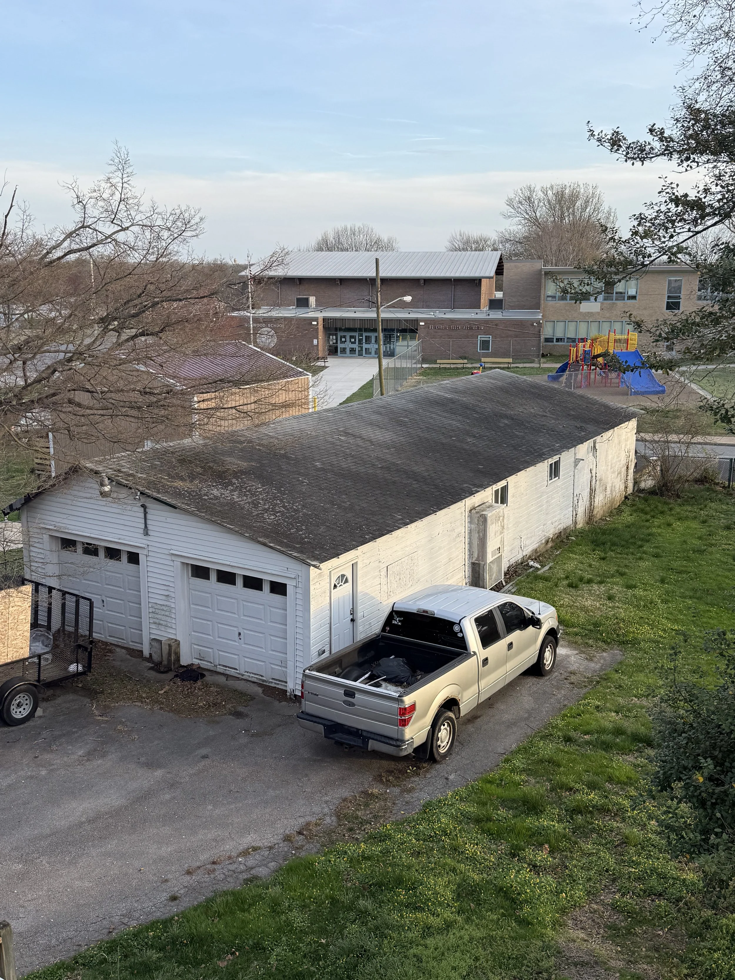 View of a backyard with a white garage, a beige truck parked outside, and a children's playground with a slide in the background.