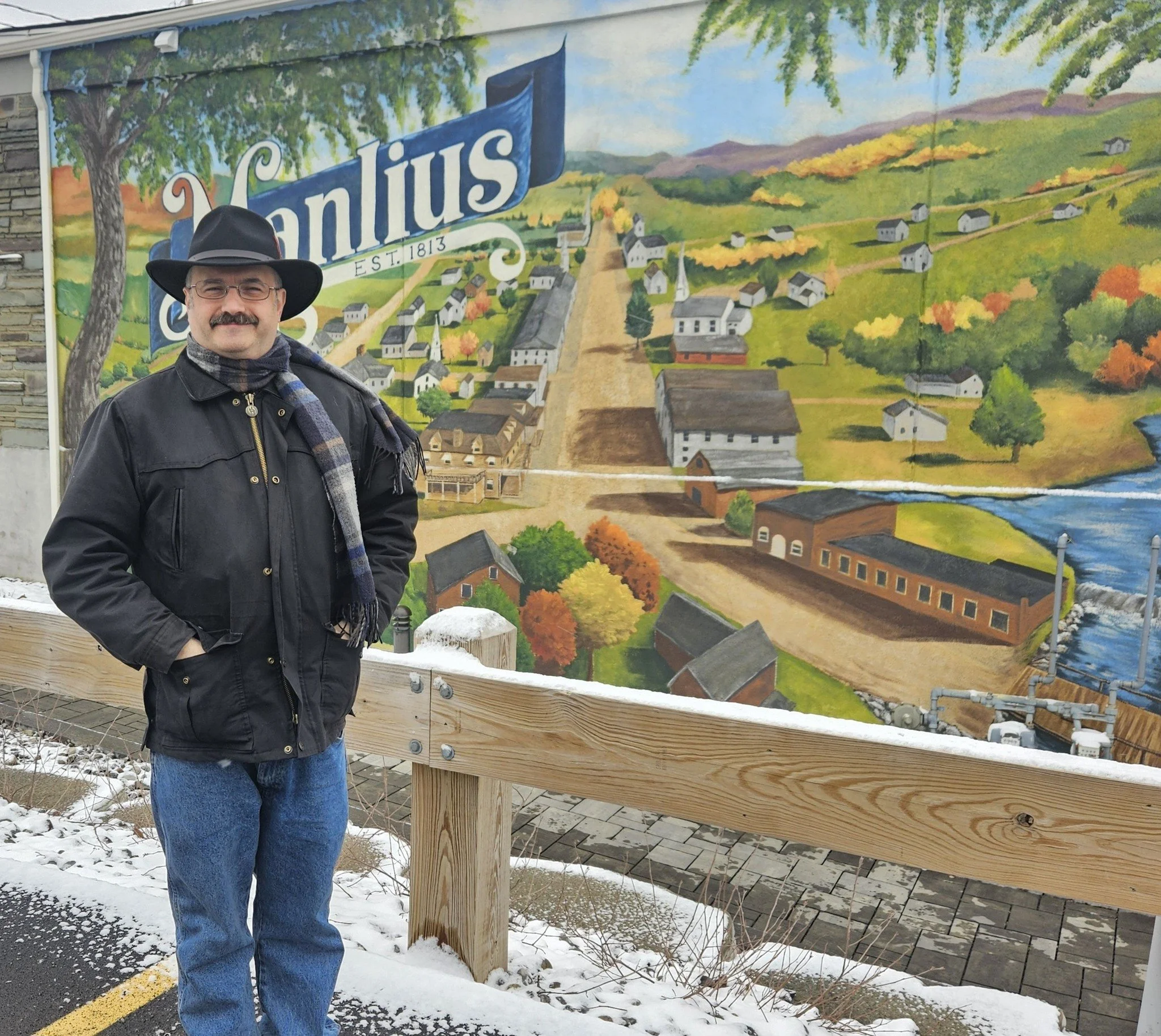 Neil J Smith standing beside a mural of the village of Manlius