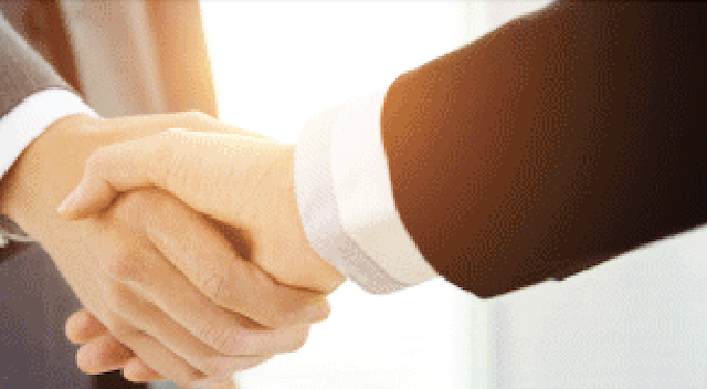Two people shaking hands, one in a white shirt and the other in a brown jacket.