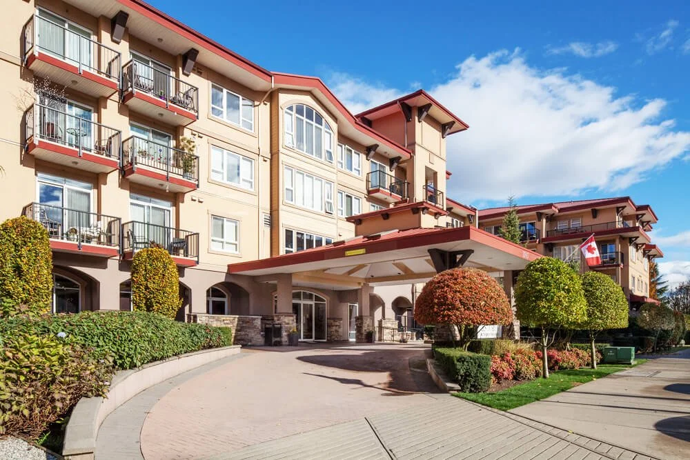 A cozy hotel lobby with sofas, armchairs, lamps, a stone fireplace, and large windows with blinds.