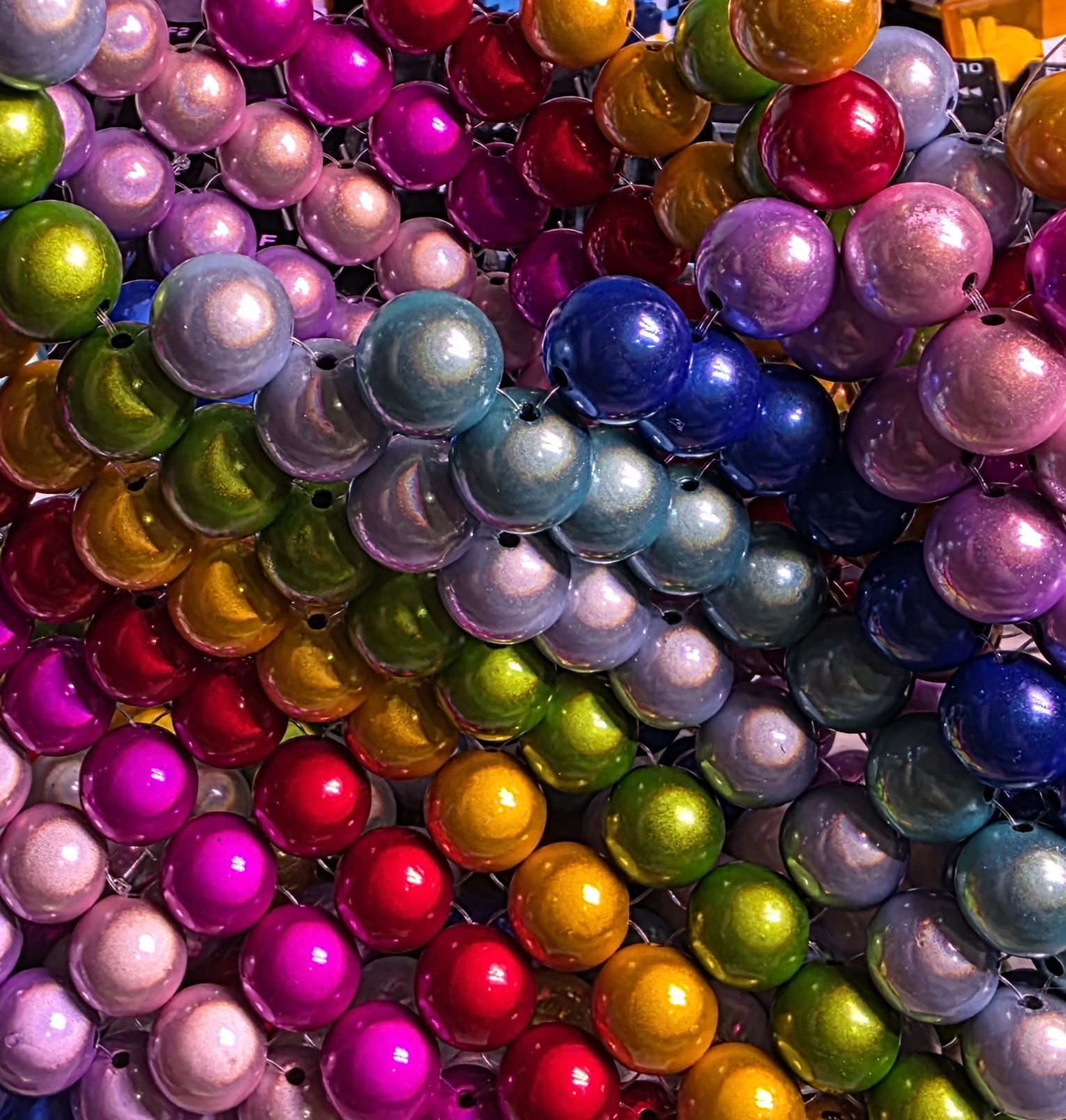 A close-up view of colorful, shiny Christmas ornaments in various colors including pink, purple, blue, green, red, gold, and silver, arranged in a dense cluster.