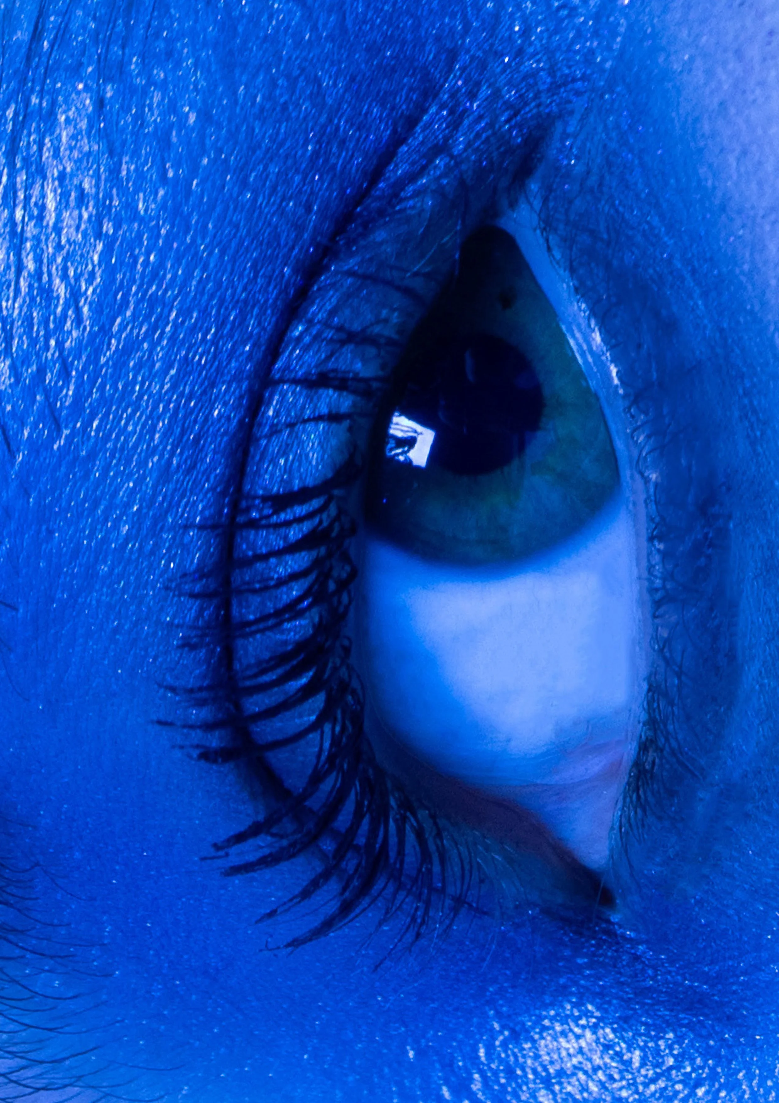 Close-up of a person's eye under blue lighting, showing the iris, eyelashes, and surrounding skin.