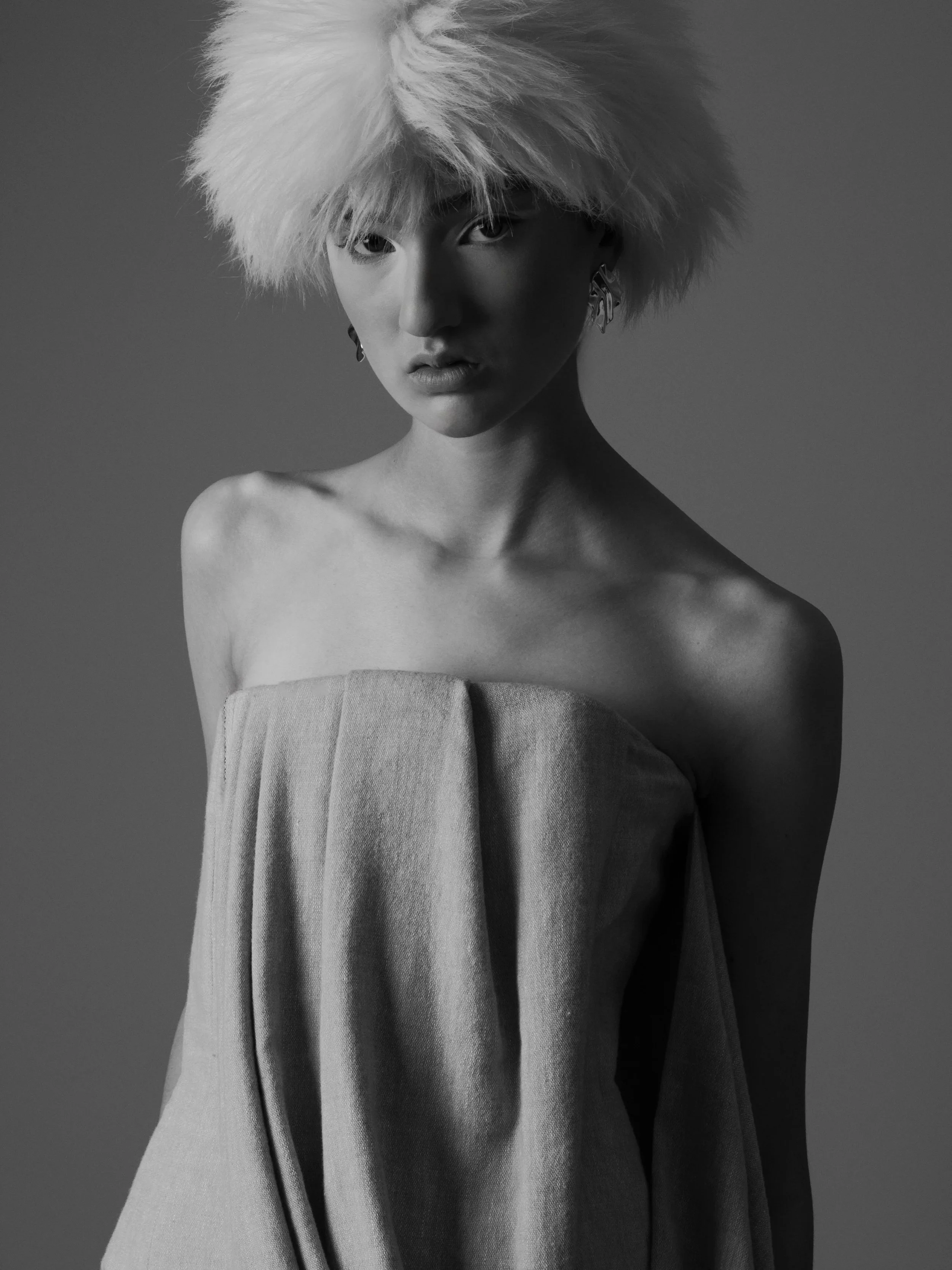 Black and white portrait of a woman with a short, spiky, platinum blonde hairstyle, wearing a strapless top and large earrings, looking directly at the camera.
