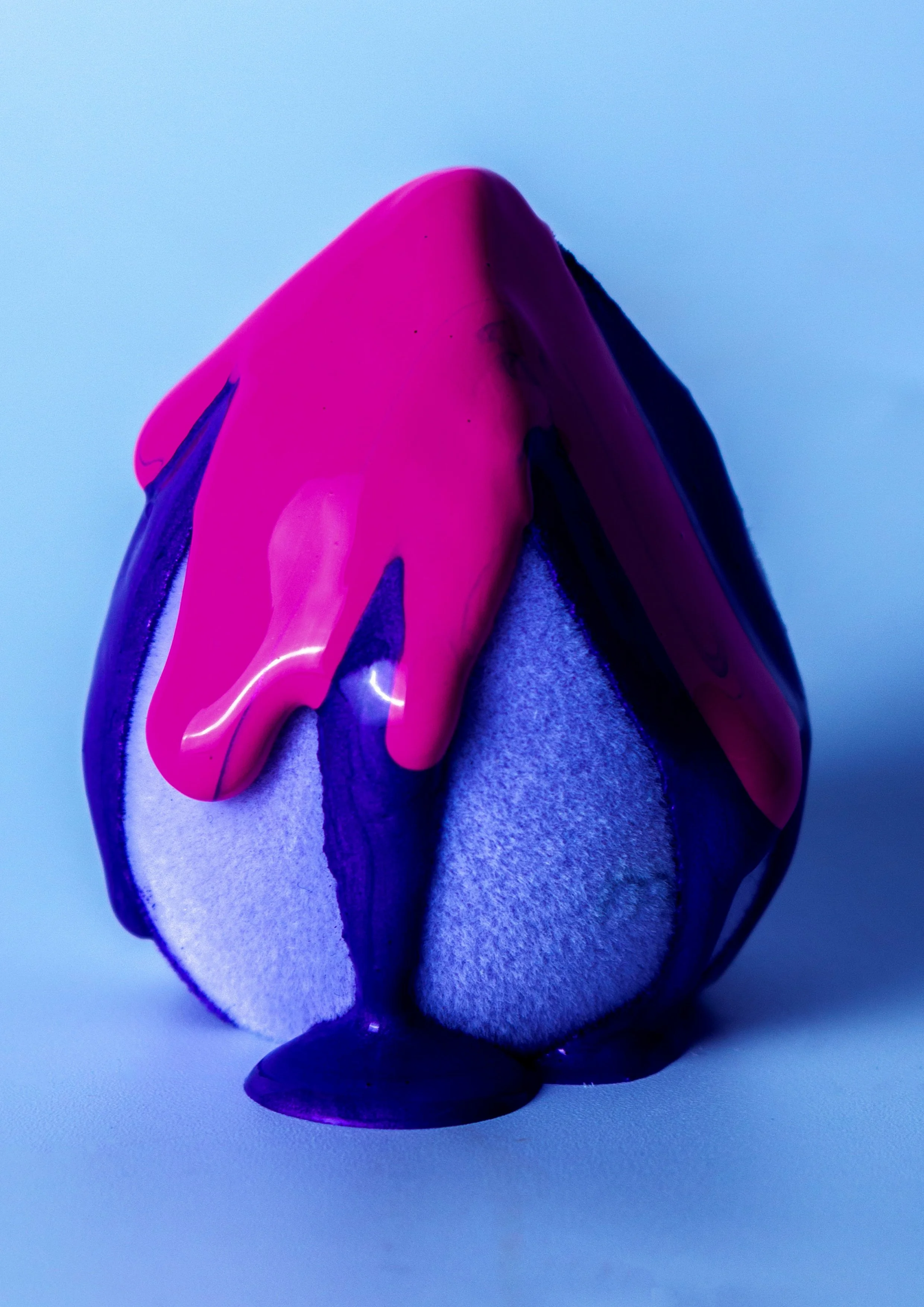 A close-up of an egg partially covered in bright pink and dark purple paint, with the paint dripping down the sides.