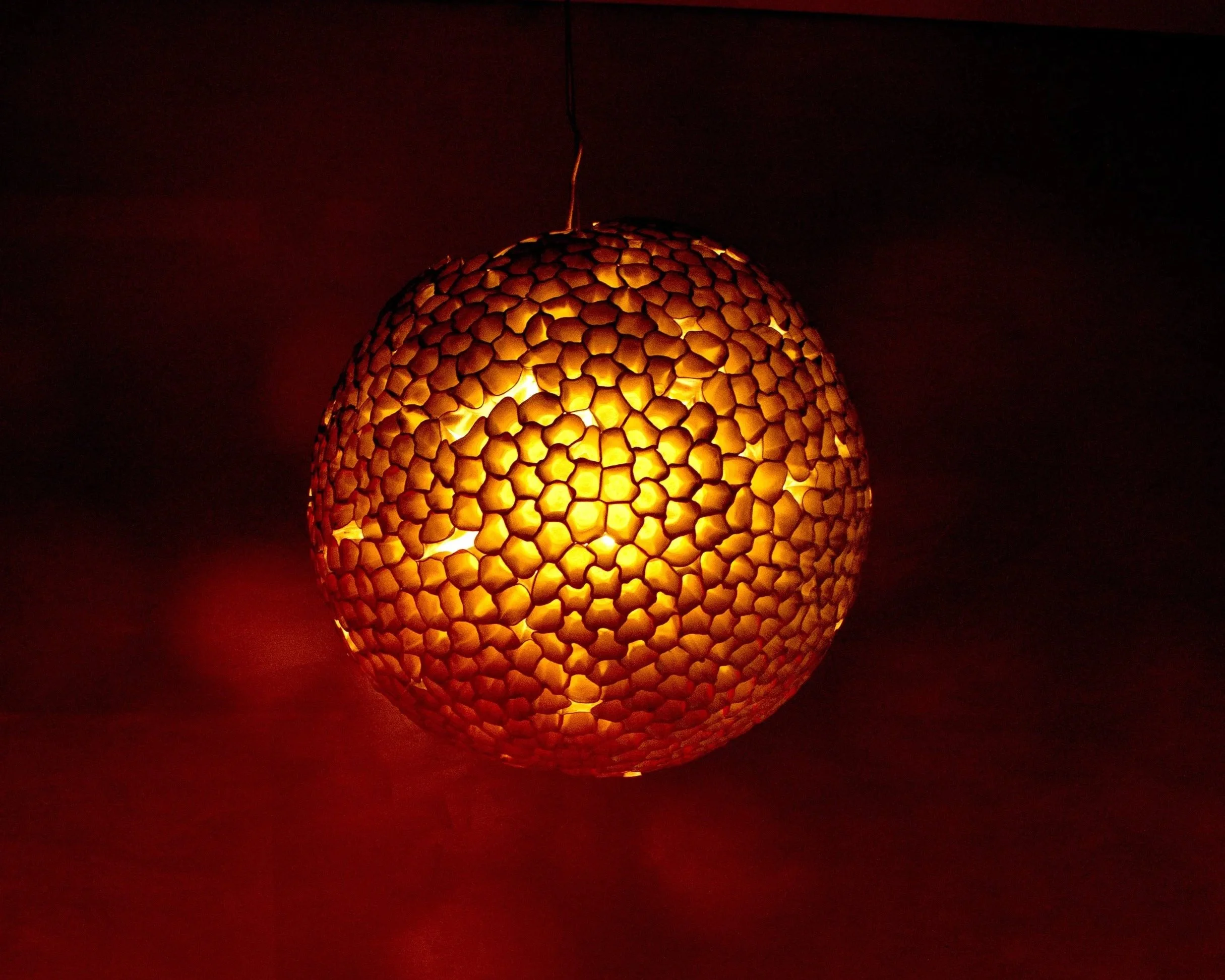 Decorative spherical lamp made of small, petal-shaped pieces, emitting warm yellow-orange light in a dark room.