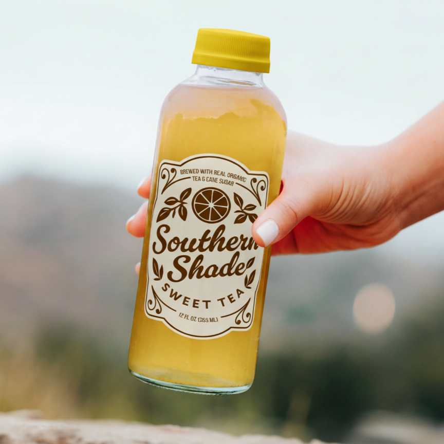 A hand holding a bottle of Southern Shade Sweet Tea with a black cap and a label that reads brewed with real organic tea and cane sugar