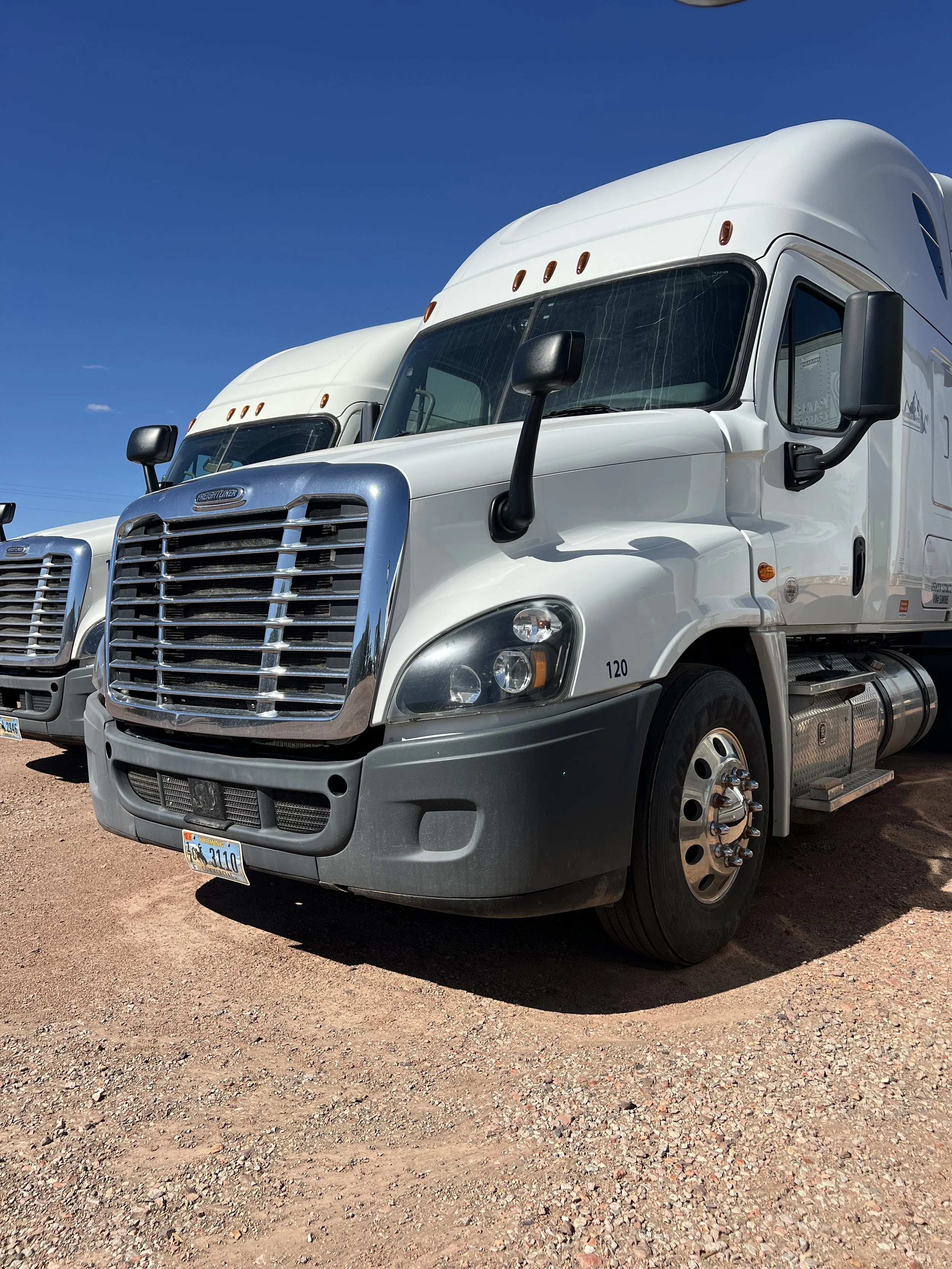 White semi-truck parked on a dirt lot under a clear blue sky.