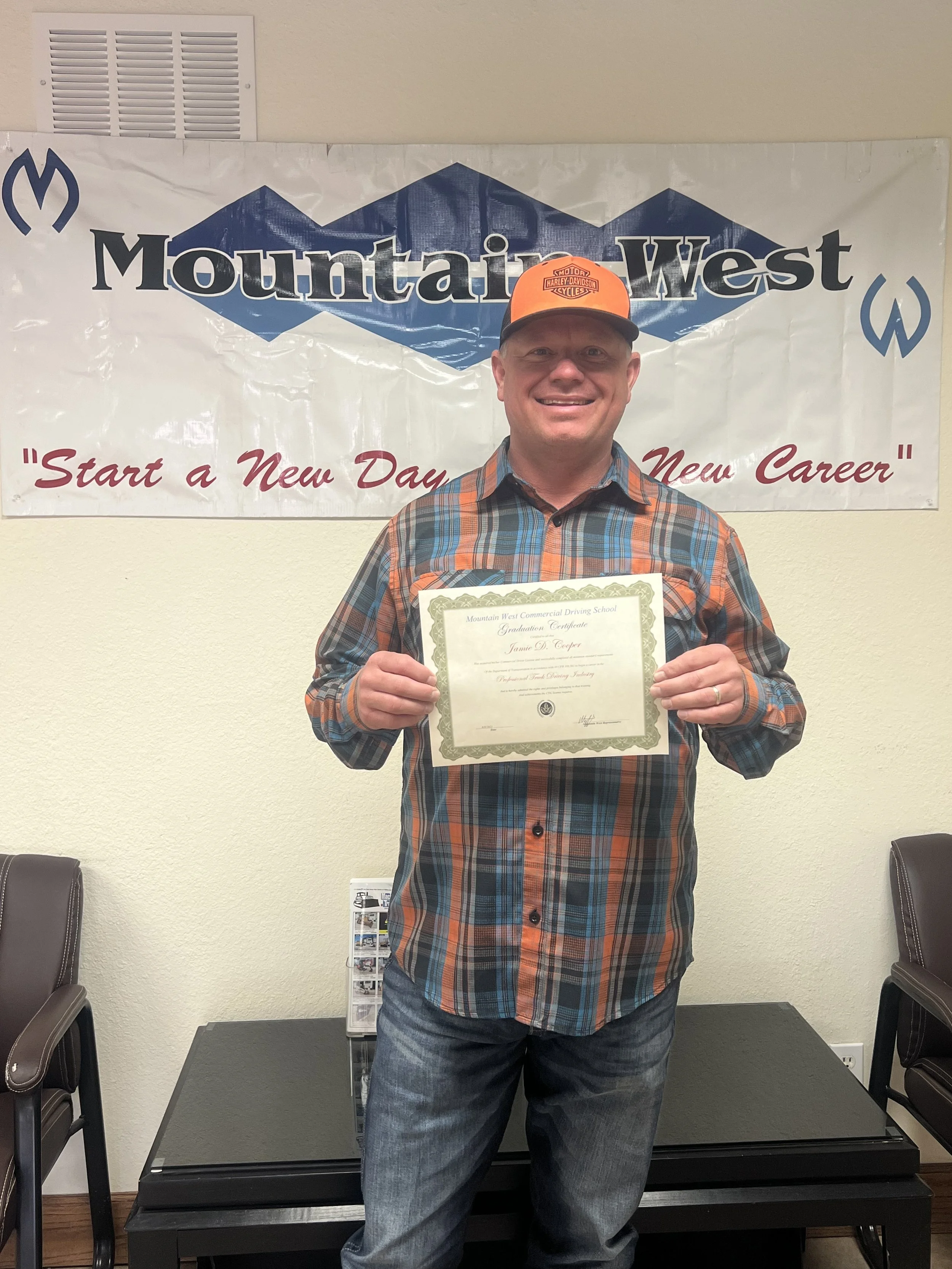 Man smiling and holding diploma in front of Mountain West banner.
