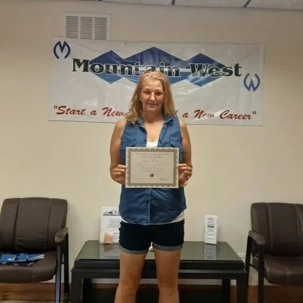 A woman holding a certificate standing in a room with a Mountaineer West banner on the wall behind her.
