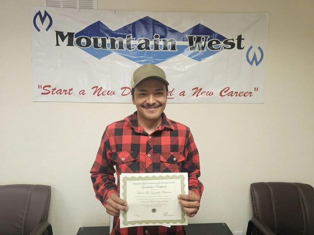 A man in a red and black checkered shirt holding a graduation certificate, standing in front of a Mountain West banner with a mountain mountain logo and the words "Start a New Degree, Start a New Career".