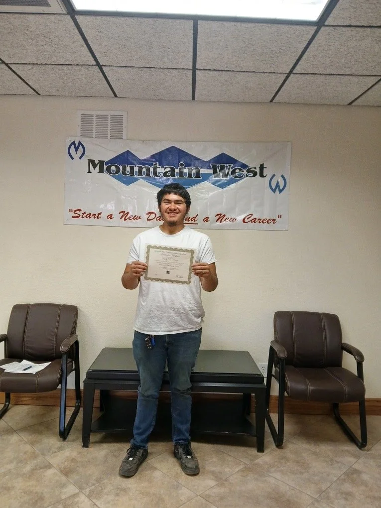 Smiling young man holding a certificate in front of a Mountain West banner at an indoor awards ceremony