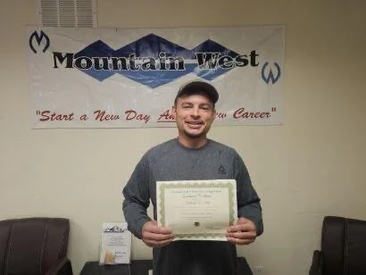 Man holding a certificate in front of a Mountain West sign and banner.