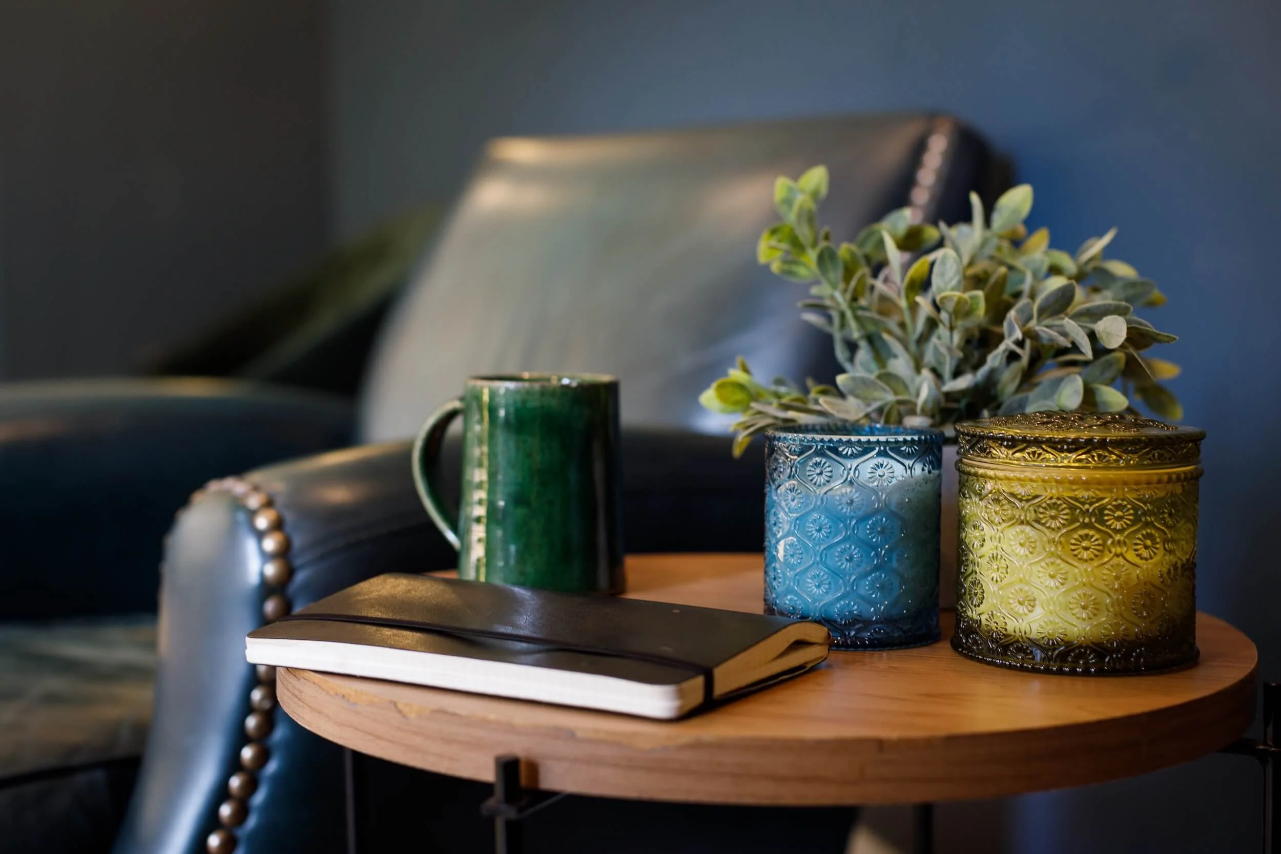 A journal and candles on a wooden side table beside a leather armchair
