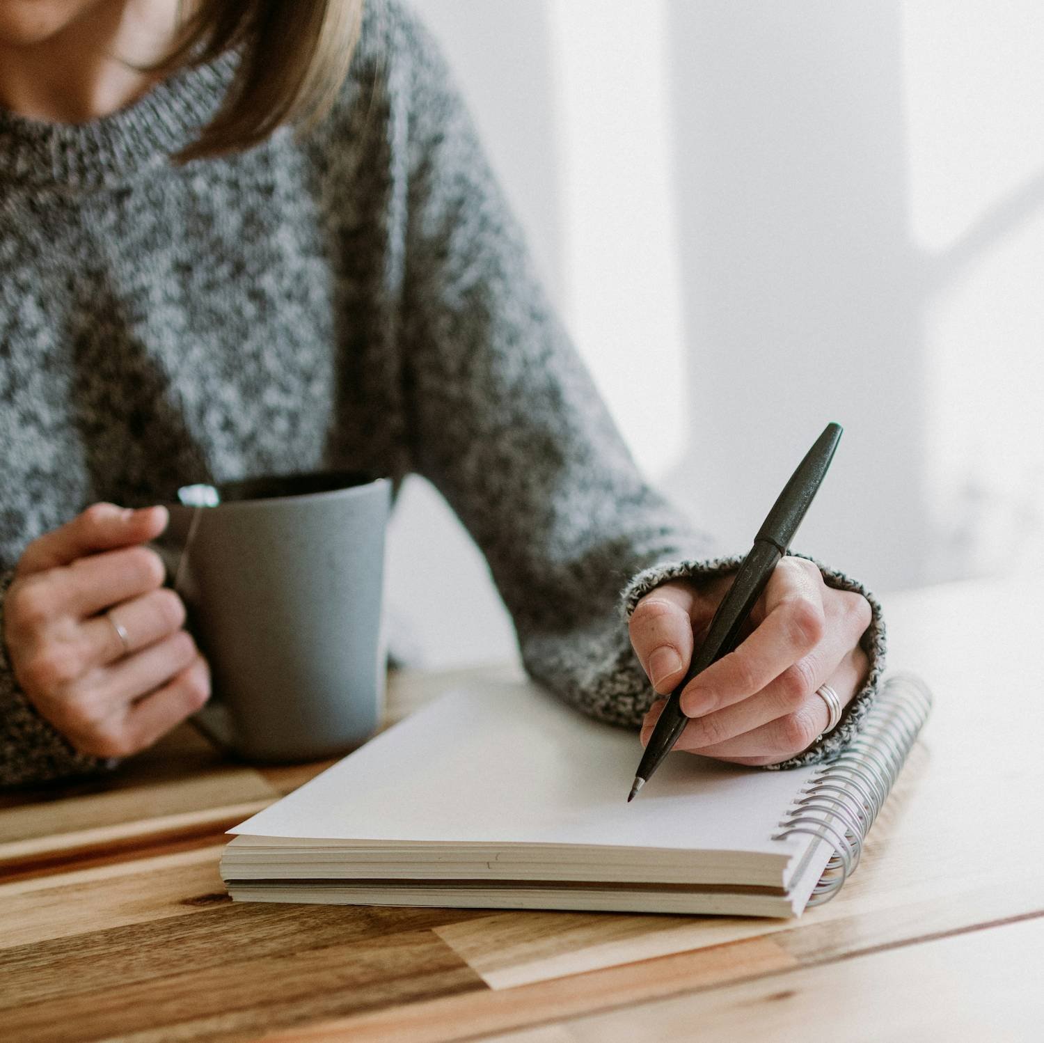 Close-up of hands writing in a notebook, reflecting self-awareness and conscious communication practice