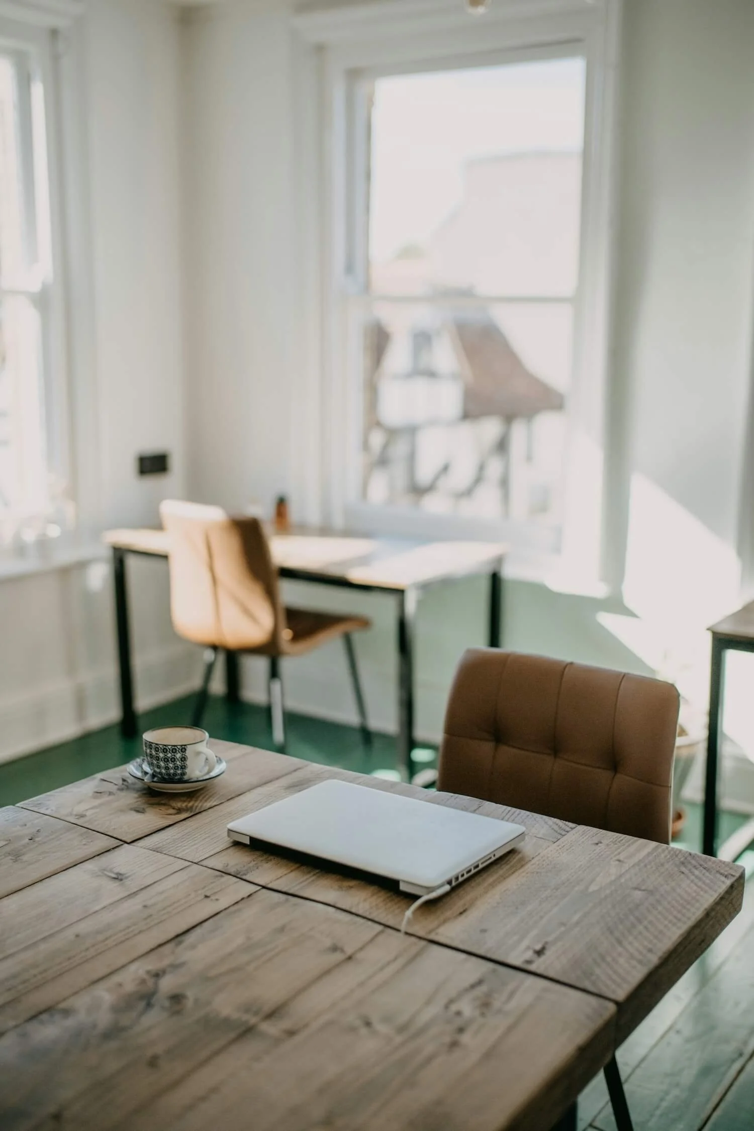 A bright, sunlit workspace with wooden tables, chairs and a laptop — setting the scene for effective communication skills in the workplace