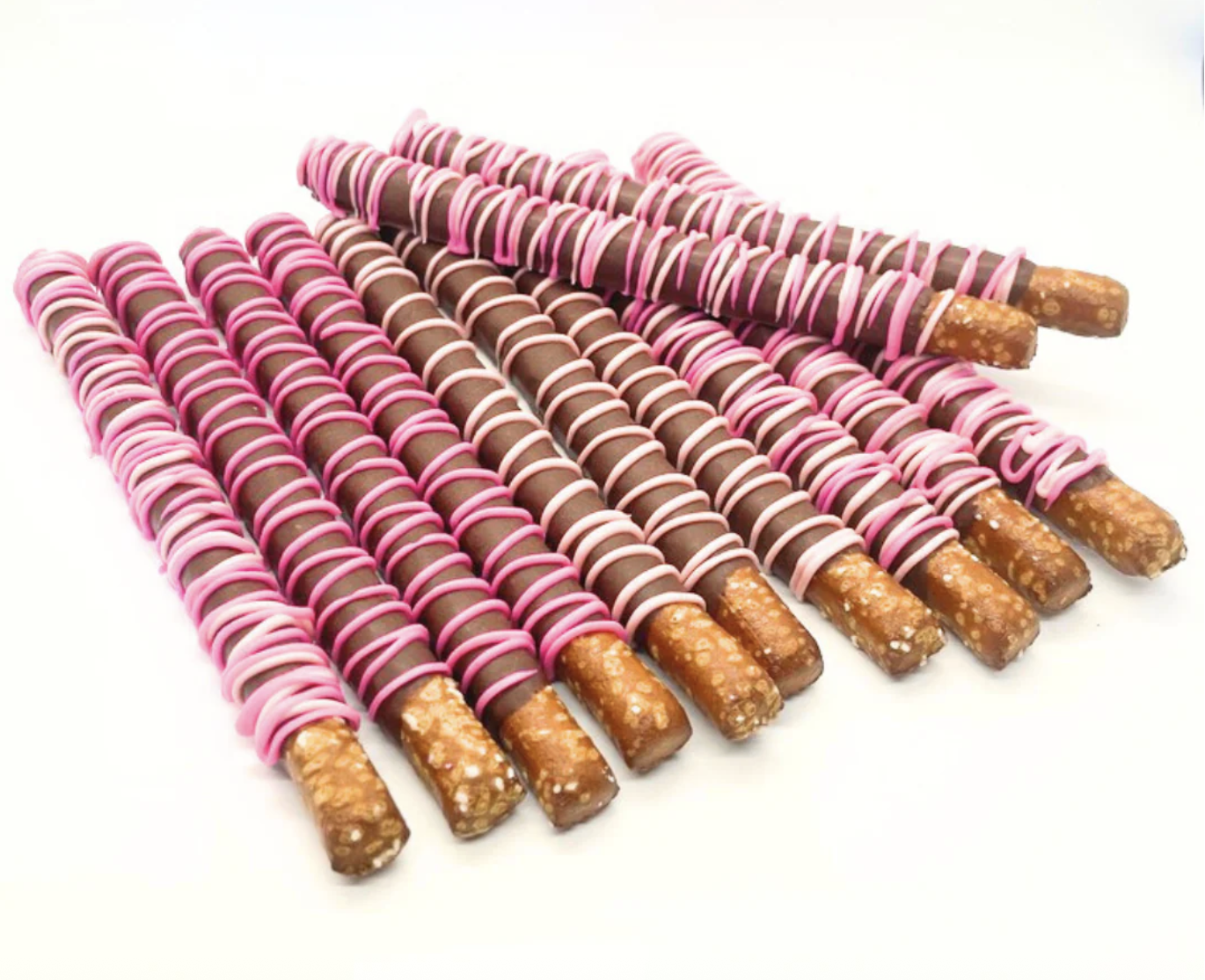 Multiple salted pretzel rods covered in milk chocolate and decorated with pink and white drizzles, arranged on a white surface.