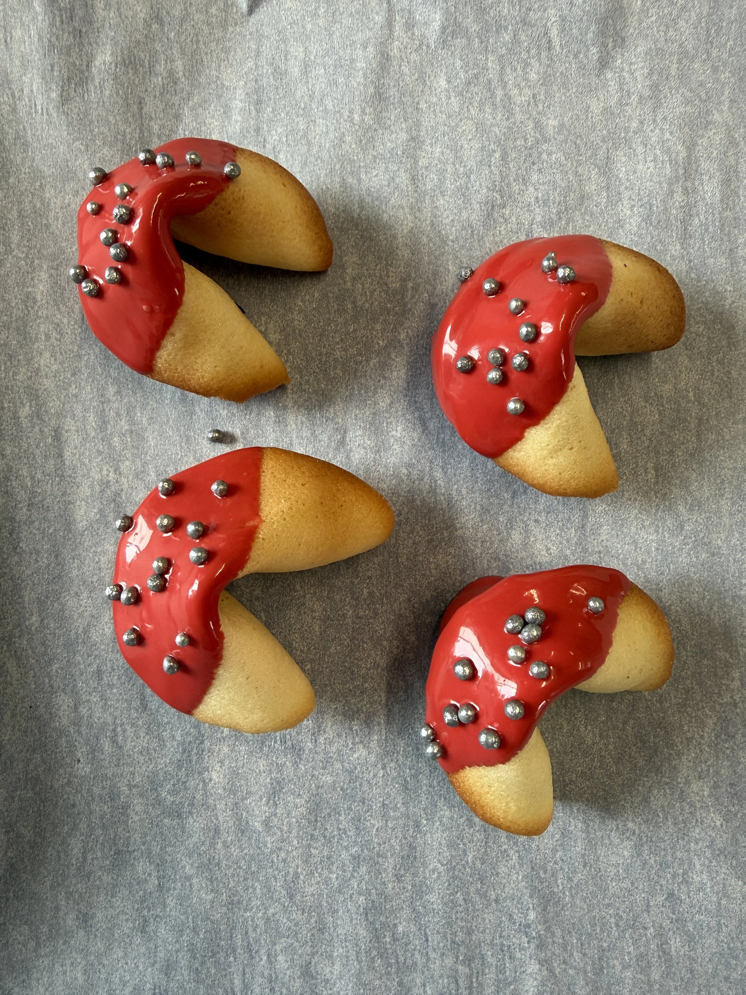 Six corporate-branded fortune cookies custom-decorated with red and silver decor on a recycled, textured surface.