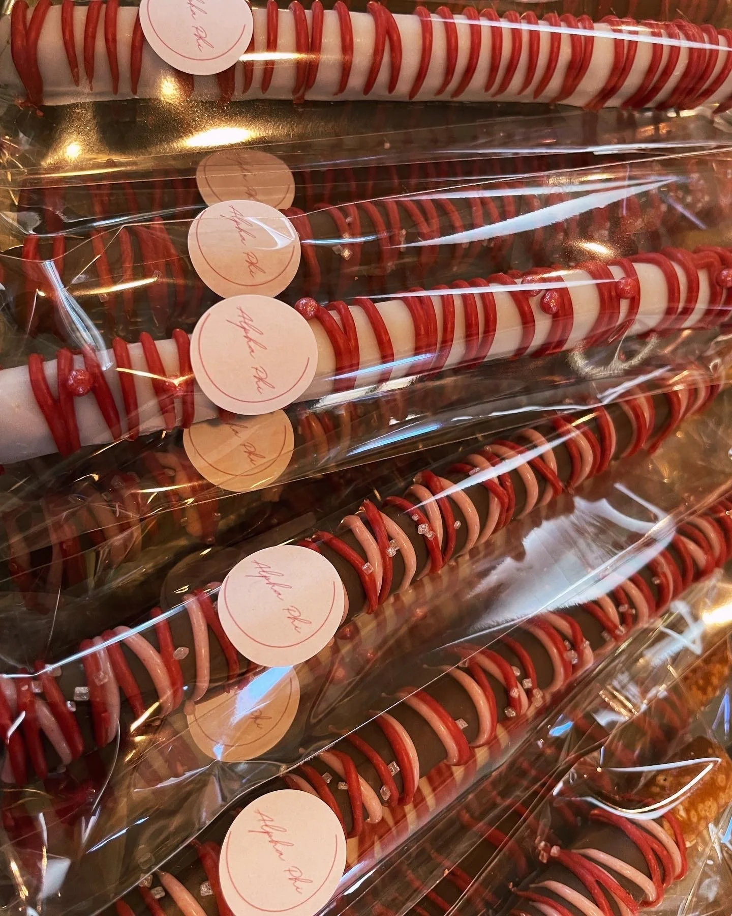 Multiple Christmas-themed candies arranged in rows, decorated with red and white icing, and wrapped in clear plastic packaging, with round labels that say "Happy Holidays."