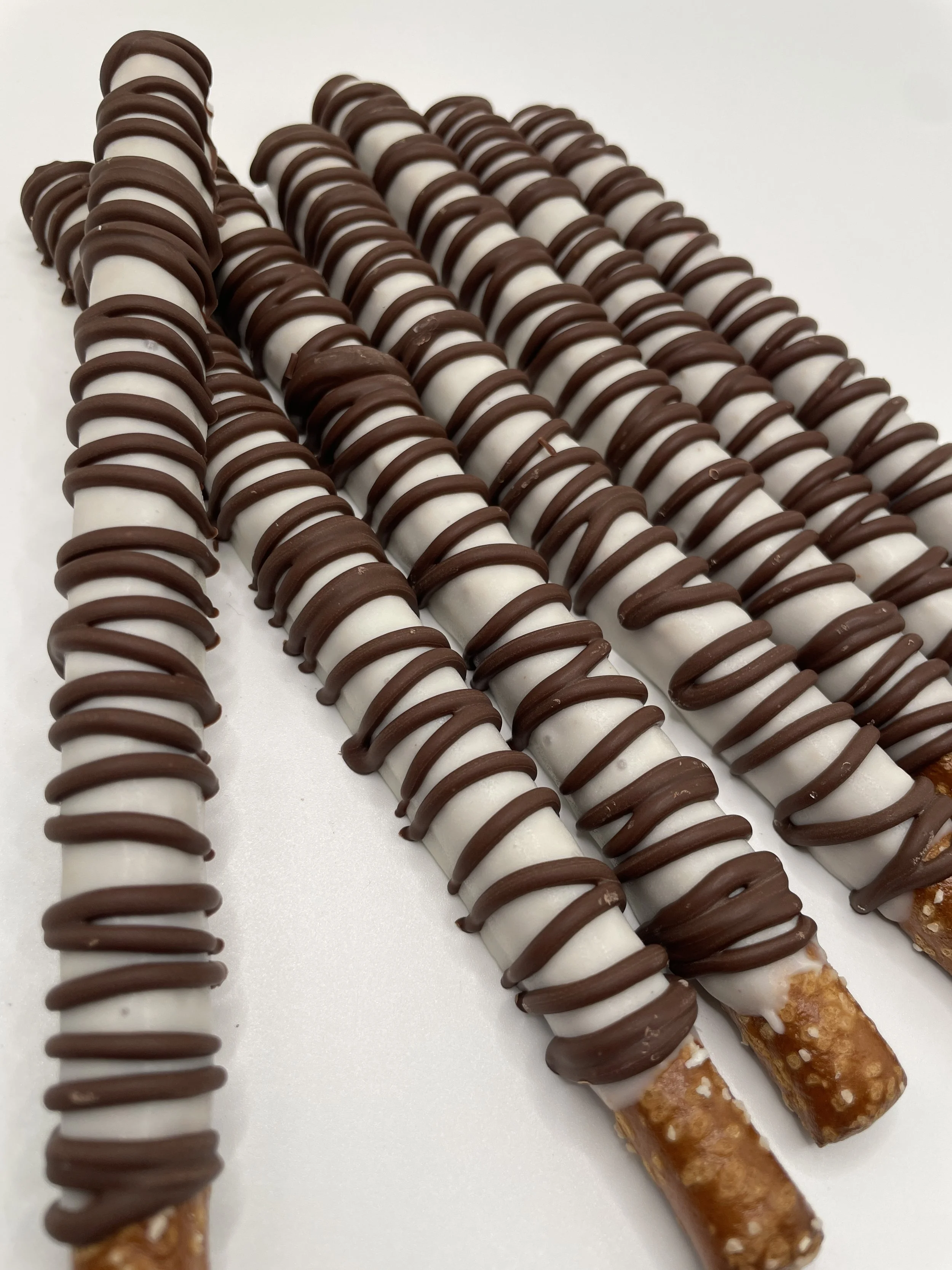 Three pretzel sticks covered with white and milk chocolate drizzle, topped with caramel and chopped nuts.