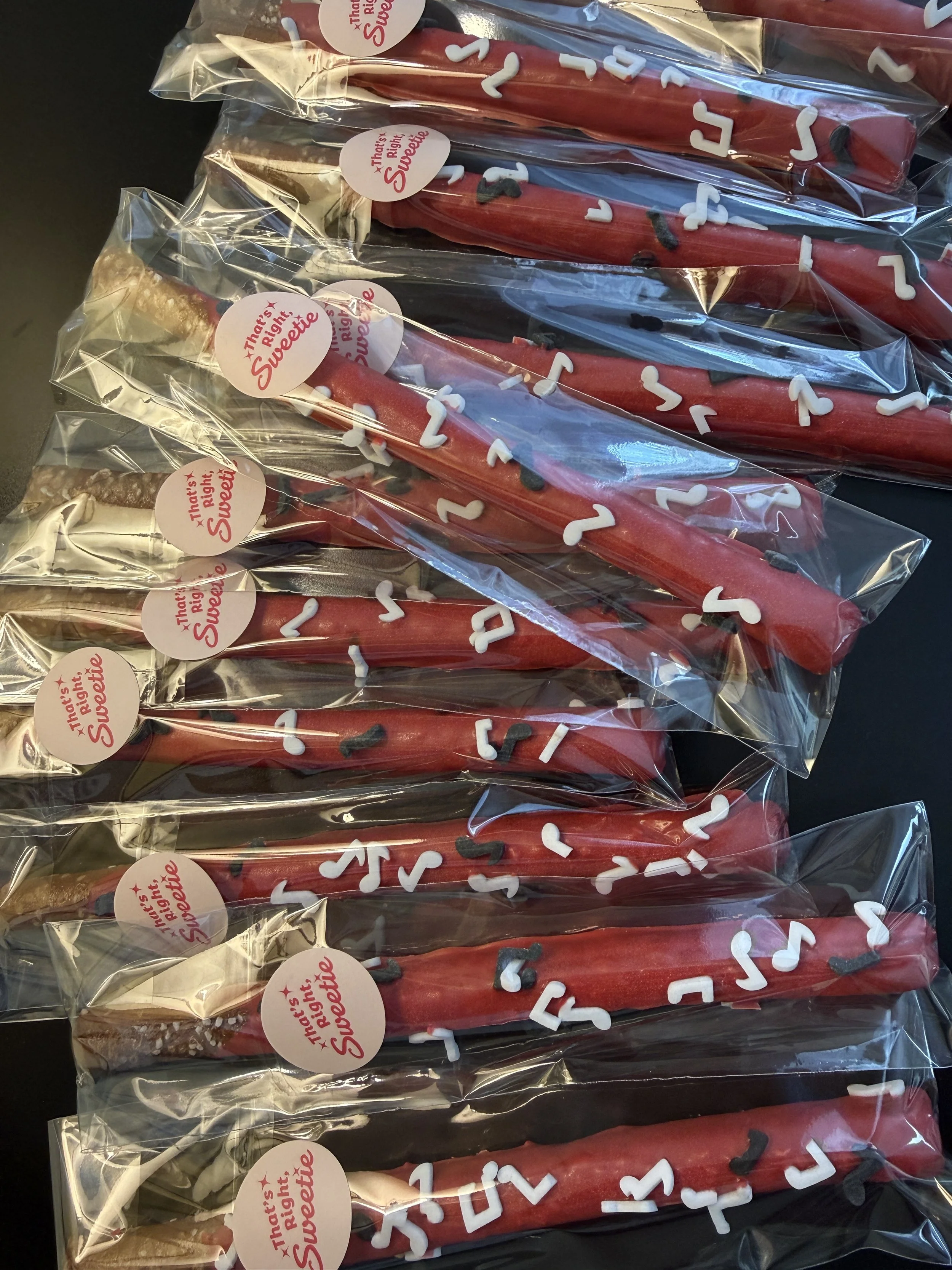 Hamburgers wrapped in clear plastic packaging with red, white, and black decorative icing or sprinkles. The packaging has a sticker that says 'That's Right, Sweetie' in red text.