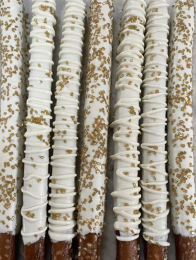 Multiple pretzel sticks covered with white chocolate and sprinkled with gold-colored sugar or sprinkles.