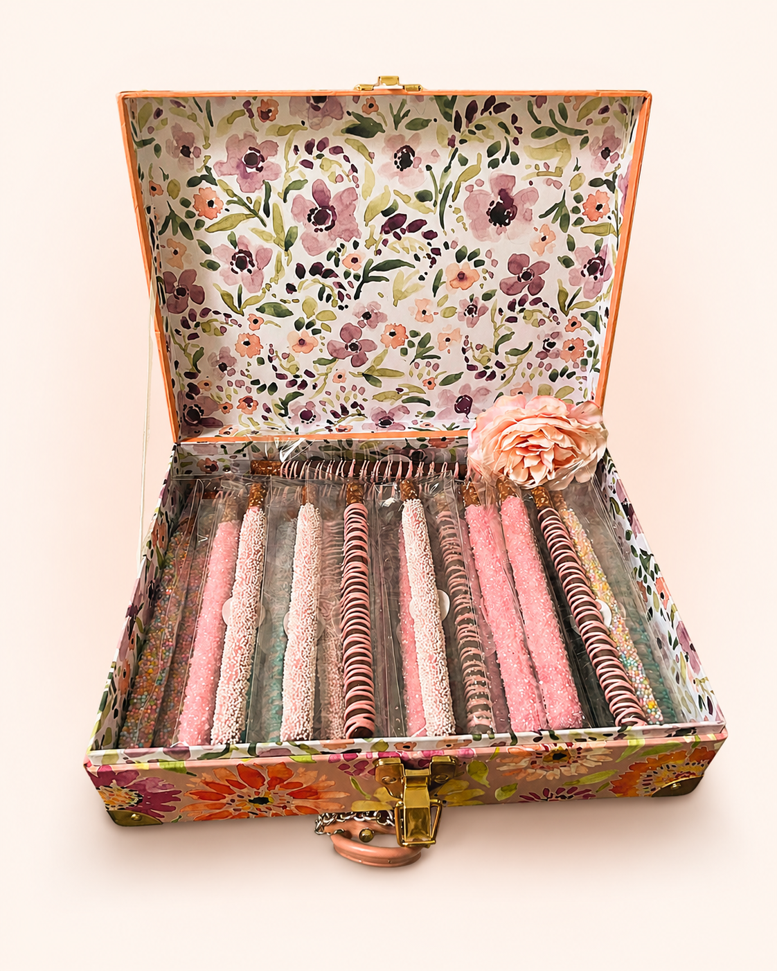 A floral-patterned box containing colorful, decorated candy sticks, with a pink flower accessory outside the candies.