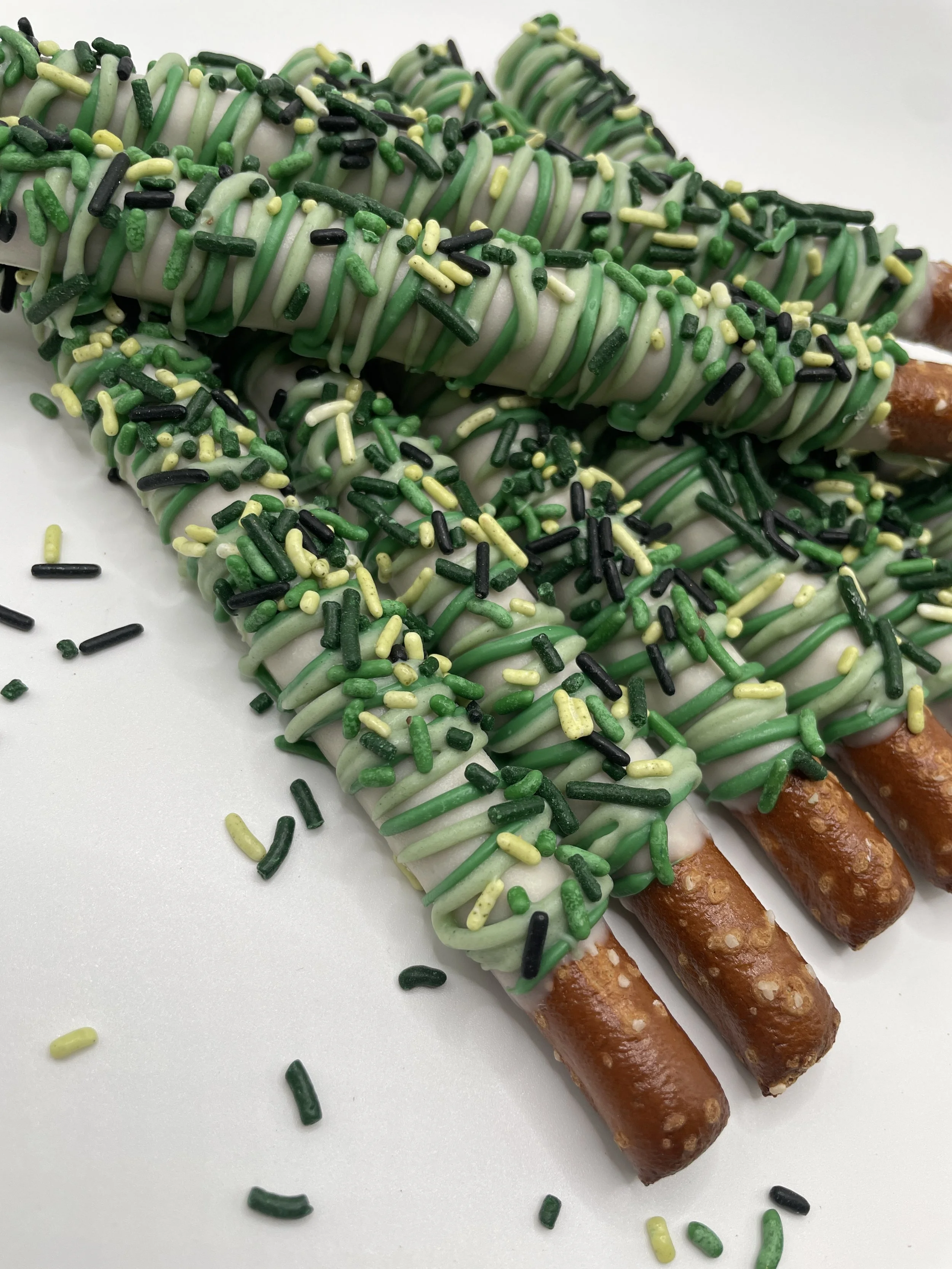 Three pretzel rods dipped in white chocolate and topped with green icing, yellow, black, and green sprinkles.