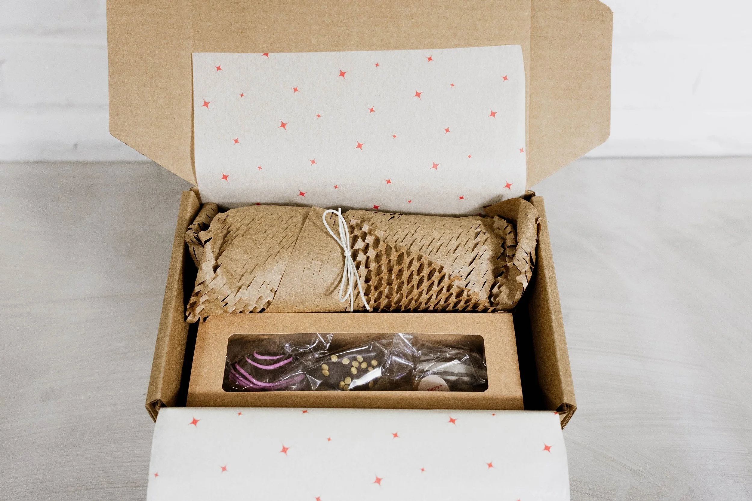 Open gift box with brown paper wrapping, tissue paper, and wrapped chocolates inside.