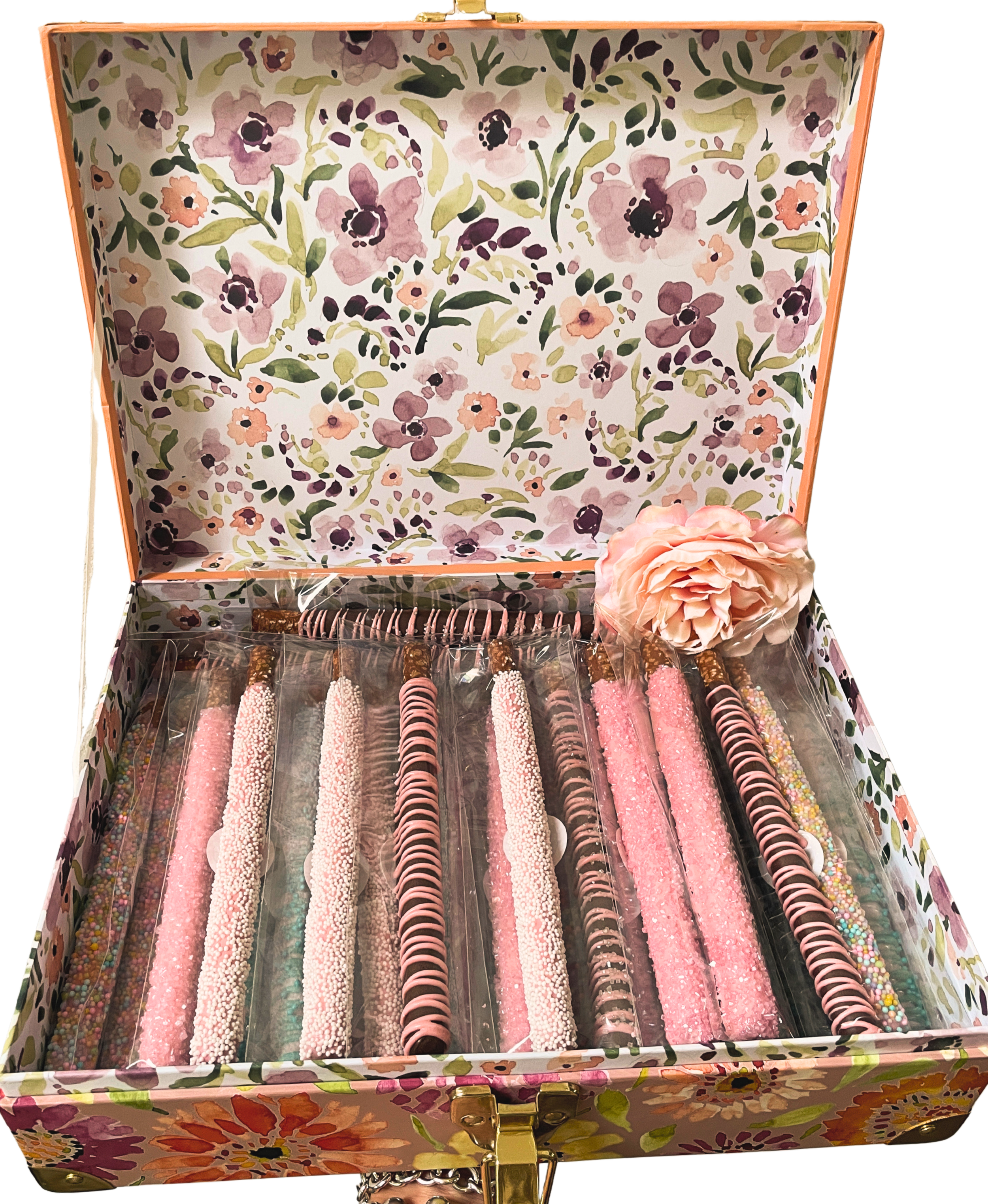 An open floral patterned jewelry box containing various pink, black, and multicolored decorated cylindrical chocolate-covered pretzels and candies.