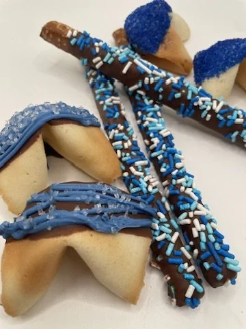 A variety of decorated pretzels and cookies with blue and brown icing, sprinkles, and sugar on a white surface.