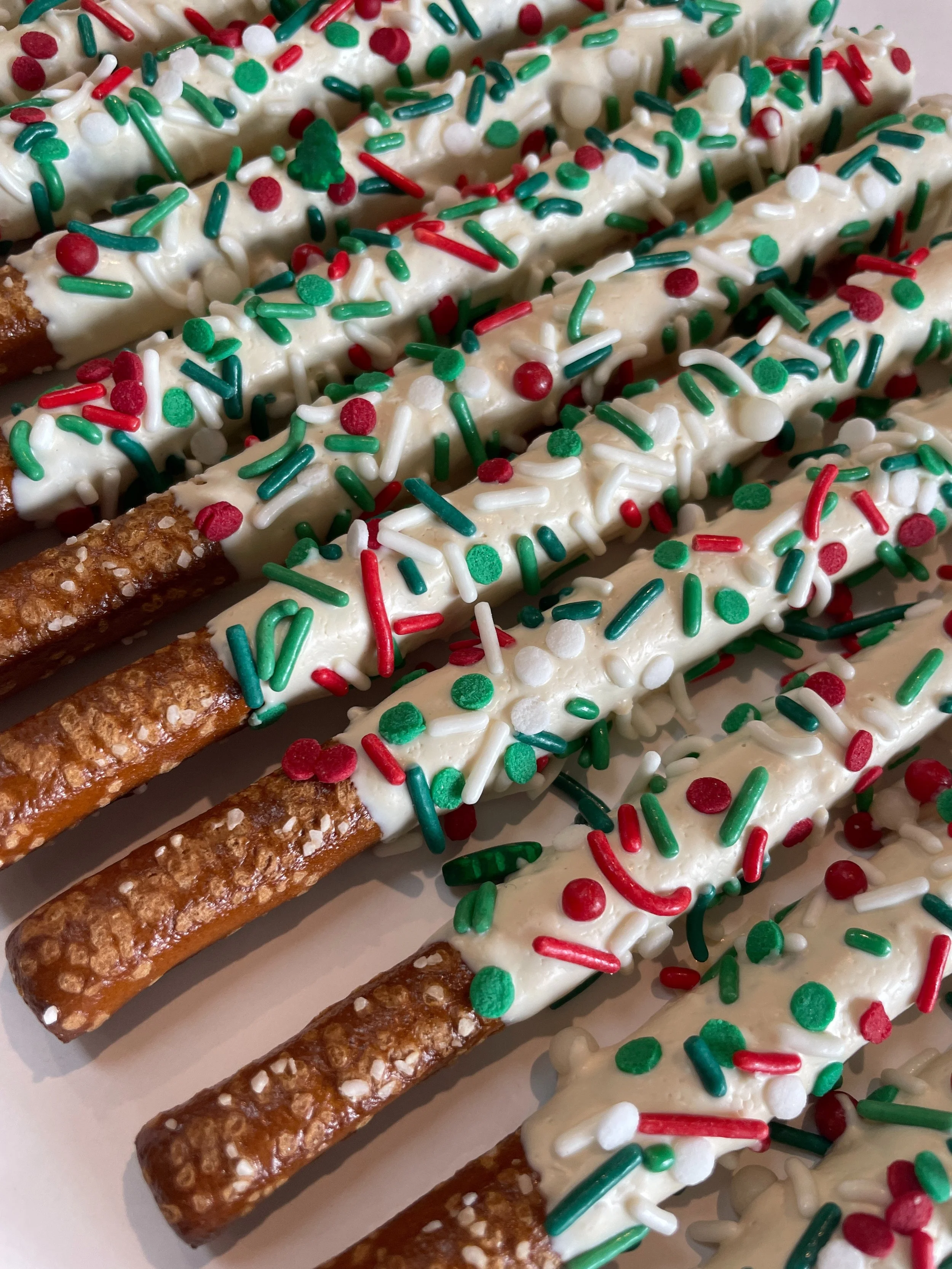 Close-up of several pretzel sticks dipped in white chocolate and decorated with red, green, and white sprinkles for a festive occasion.