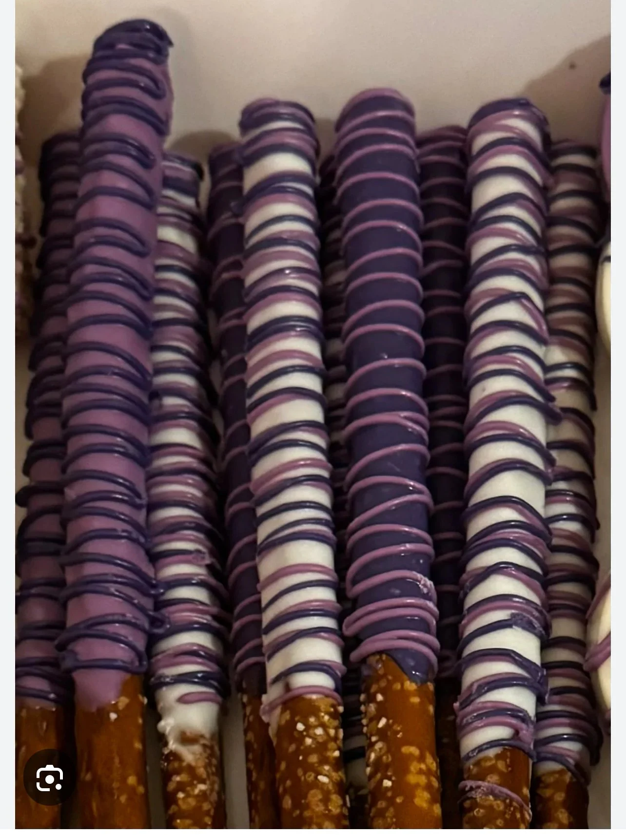 Multiple pretzel rods glazed in chocolate with purple, white, and dark drizzle toppings, arranged side by side.