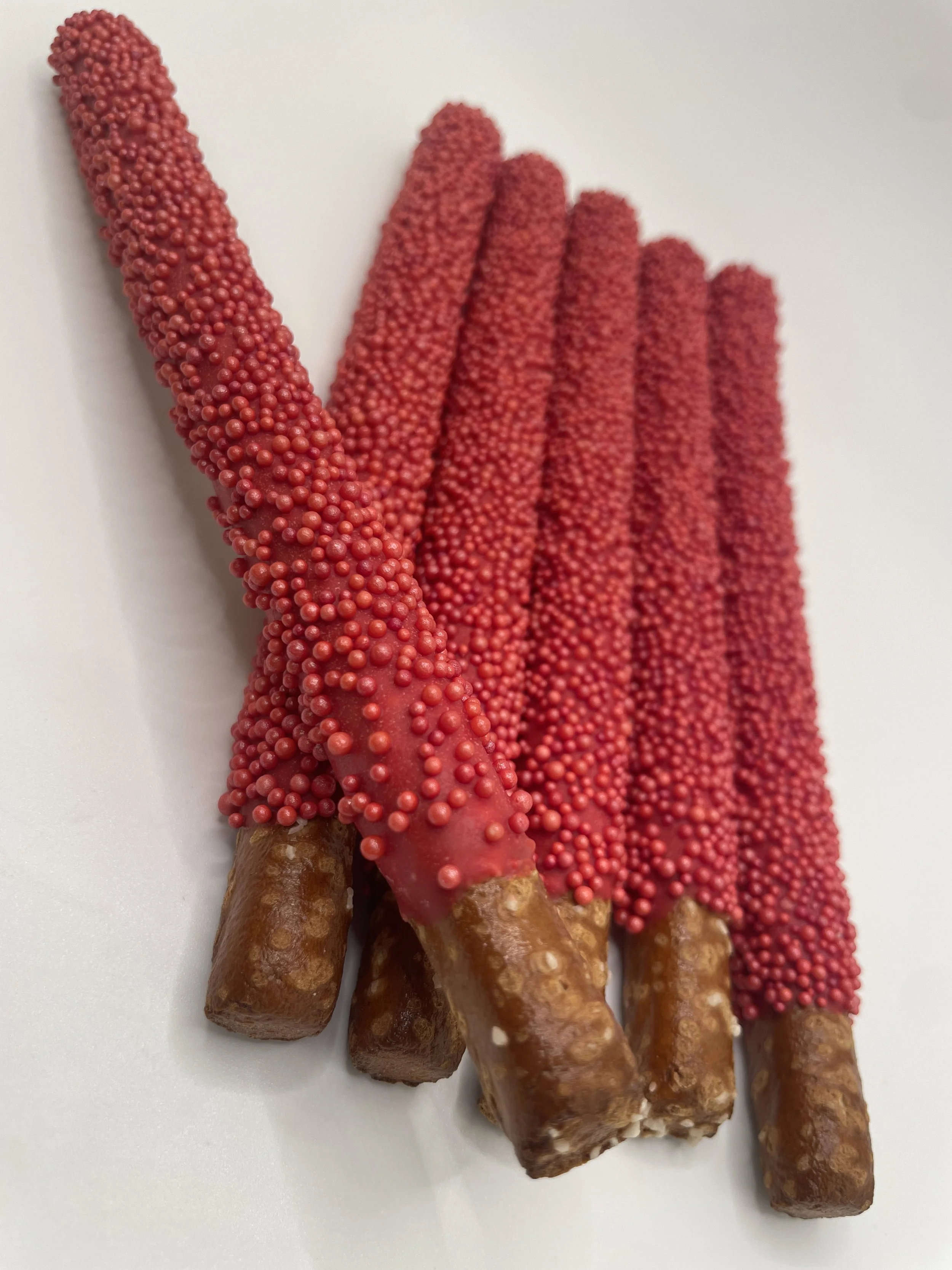 Five pretzel sticks dipped in red chocolate and coated with red nonpareil sprinkles.