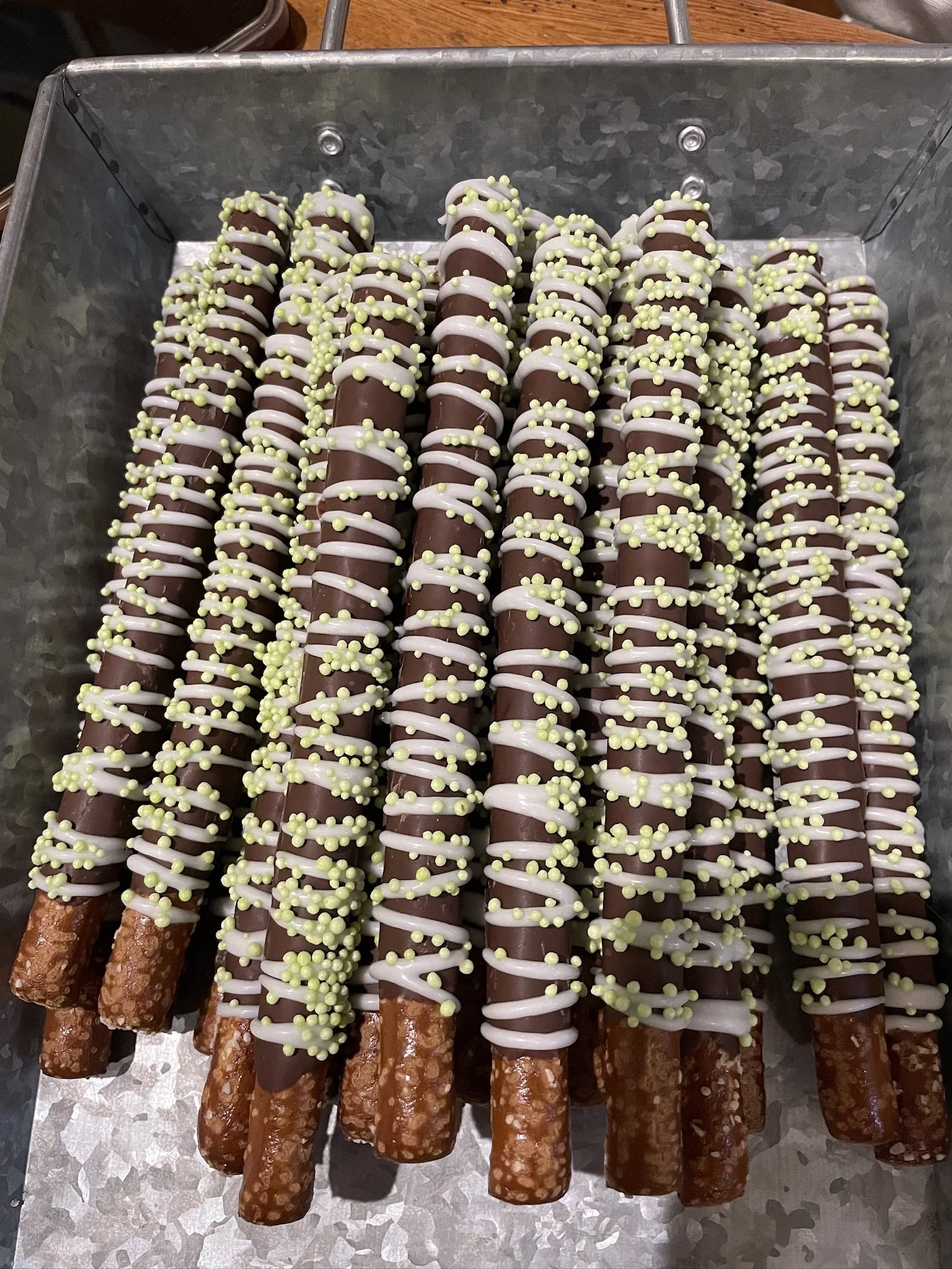 Chocolate-dipped pretzels with white and yellow sprinkles arranged in a metal tray.