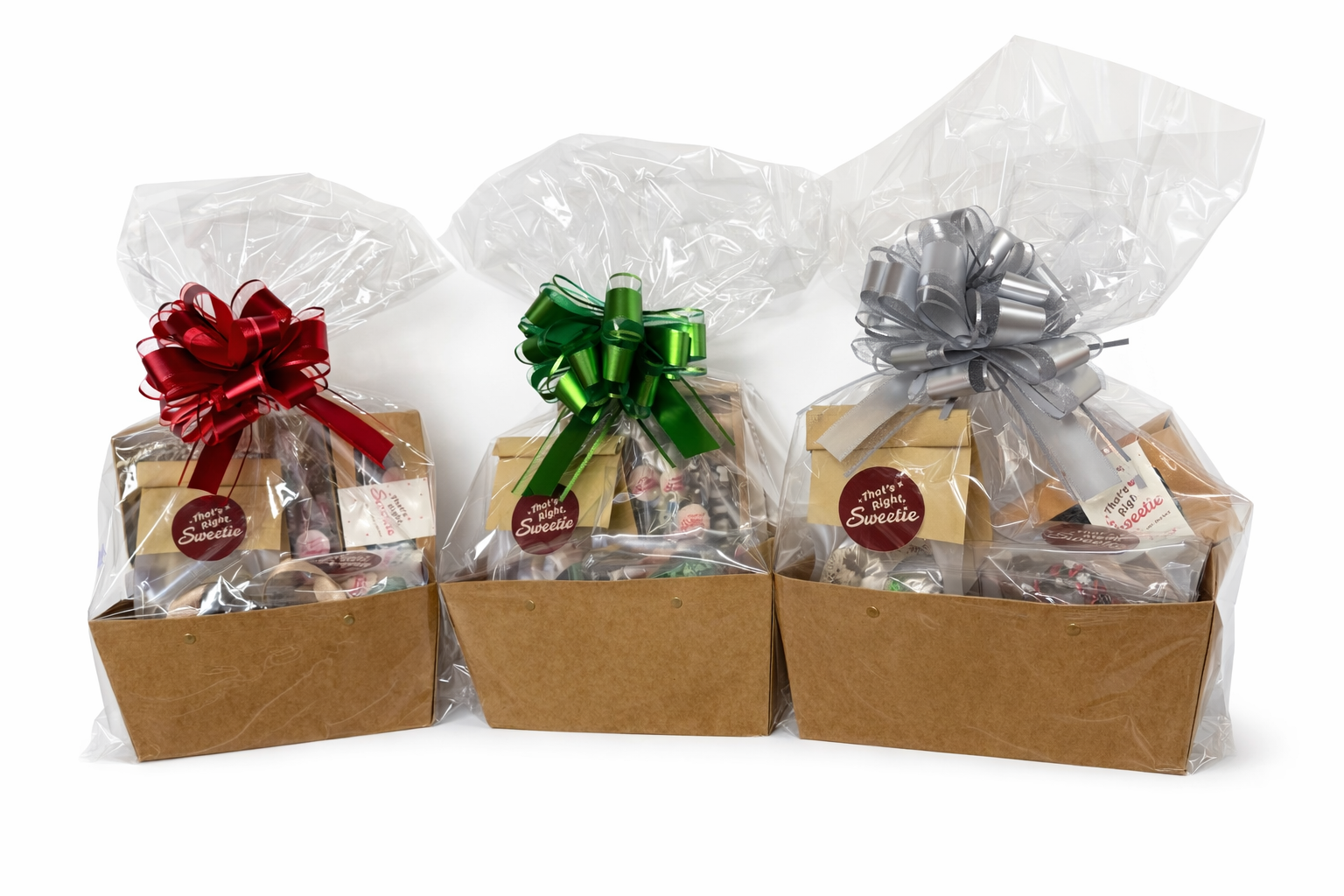Three gift baskets wrapped in clear plastic with decorative bows in red, green, and silver, containing assorted candies and chocolates.