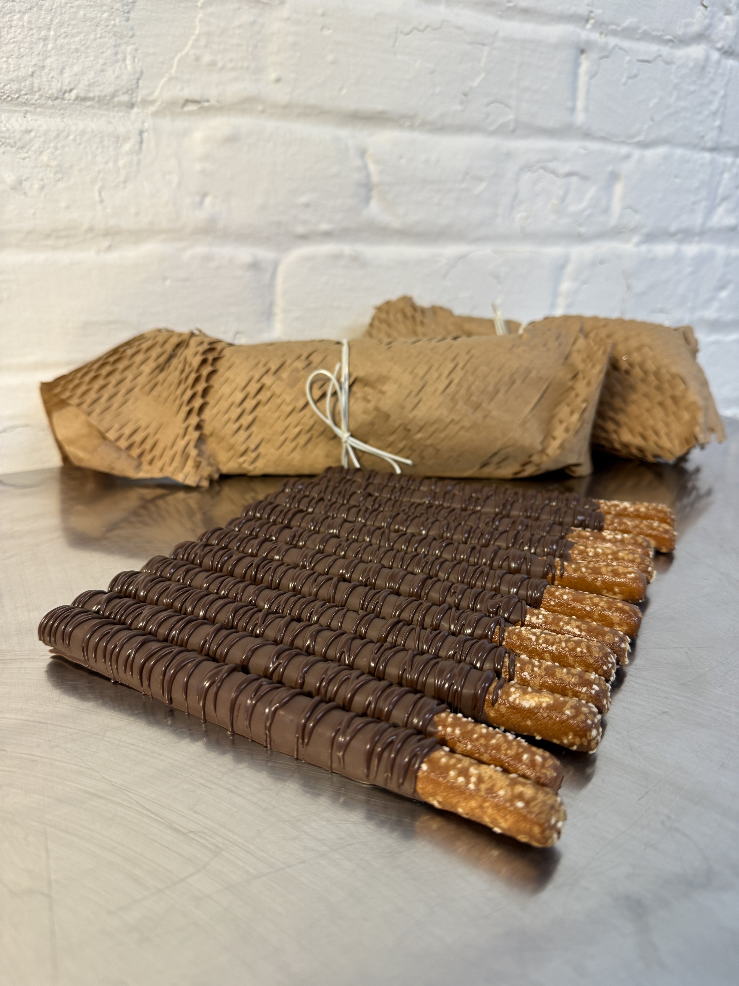 Chocolate-dipped pretzel sticks arranged in a row on a metal surface.