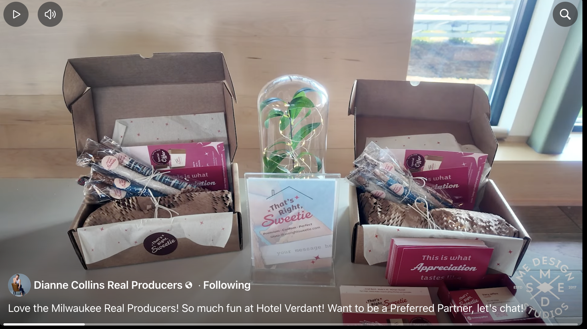 Open boxes with pink promotional brochures, small wrapped items, a small potted plant under a glass dome, and a sign from Hotel Verdant on a table near a window.