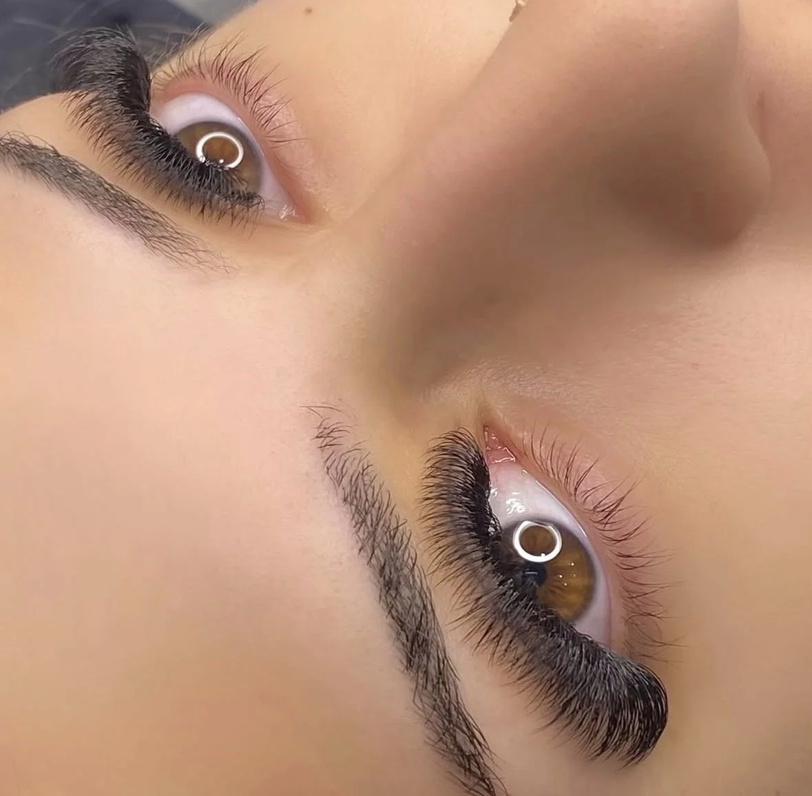 Close-up of a person's upside-down face with brown eyes, long eyelashes, and full eyebrows, focusing on eyes and nose.
