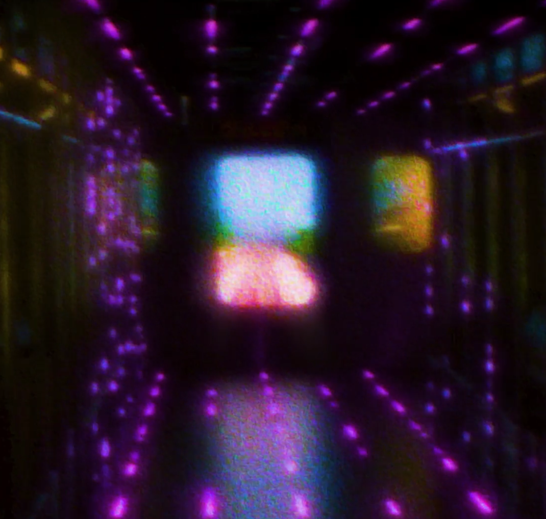 A dark hallway illuminated by purple, blue, and yellow neon lights, creating a tunnel-like effect with a bright screen or opening at the end.